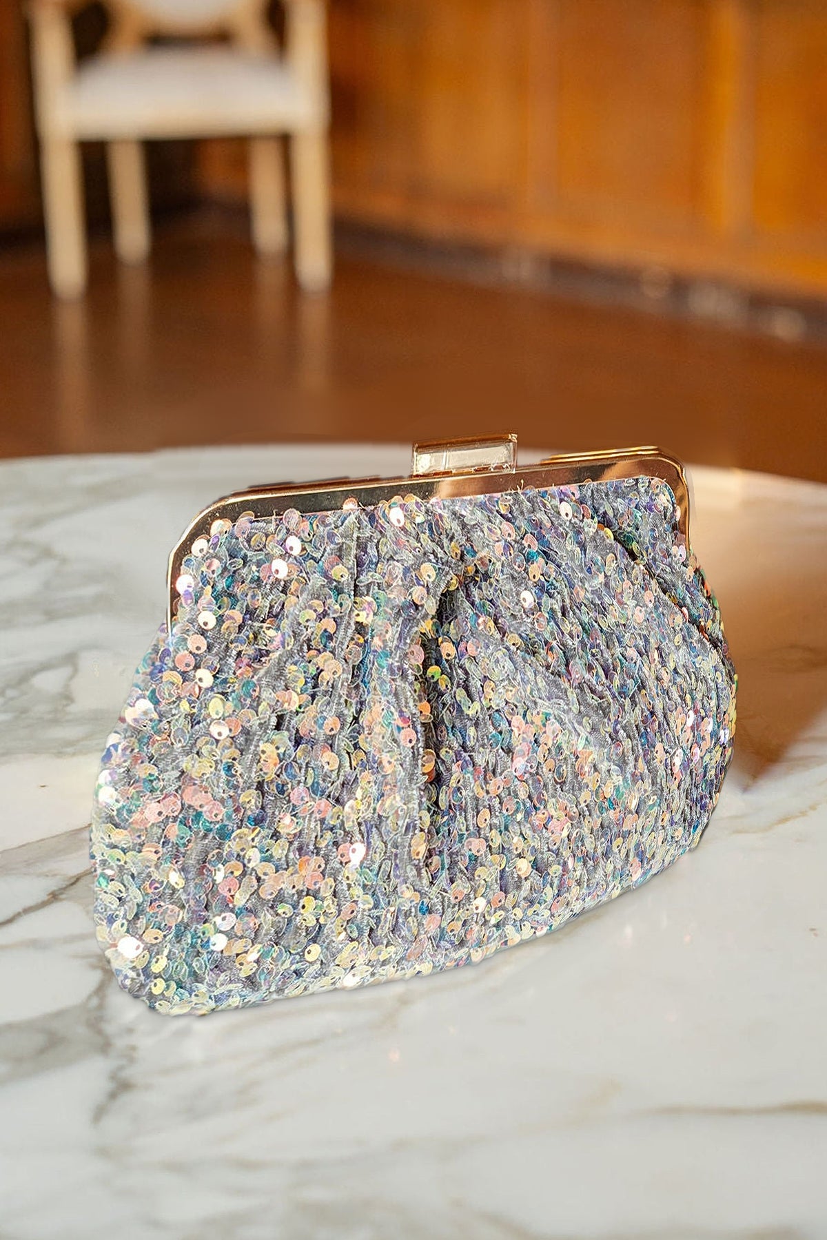 The Trixie sequin clutch with its gold frame on a marble table.