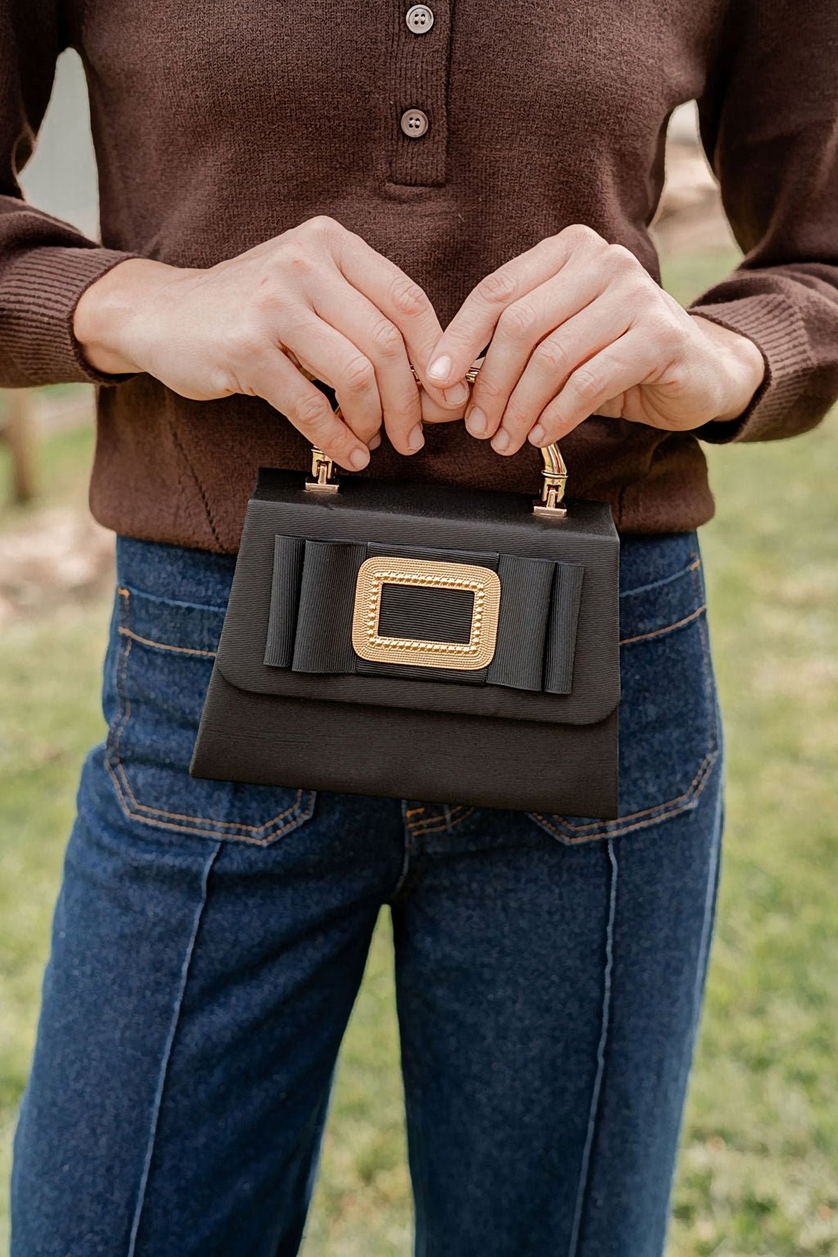 The Black Lulu bag held by its handle with a brown sweater and jeans.