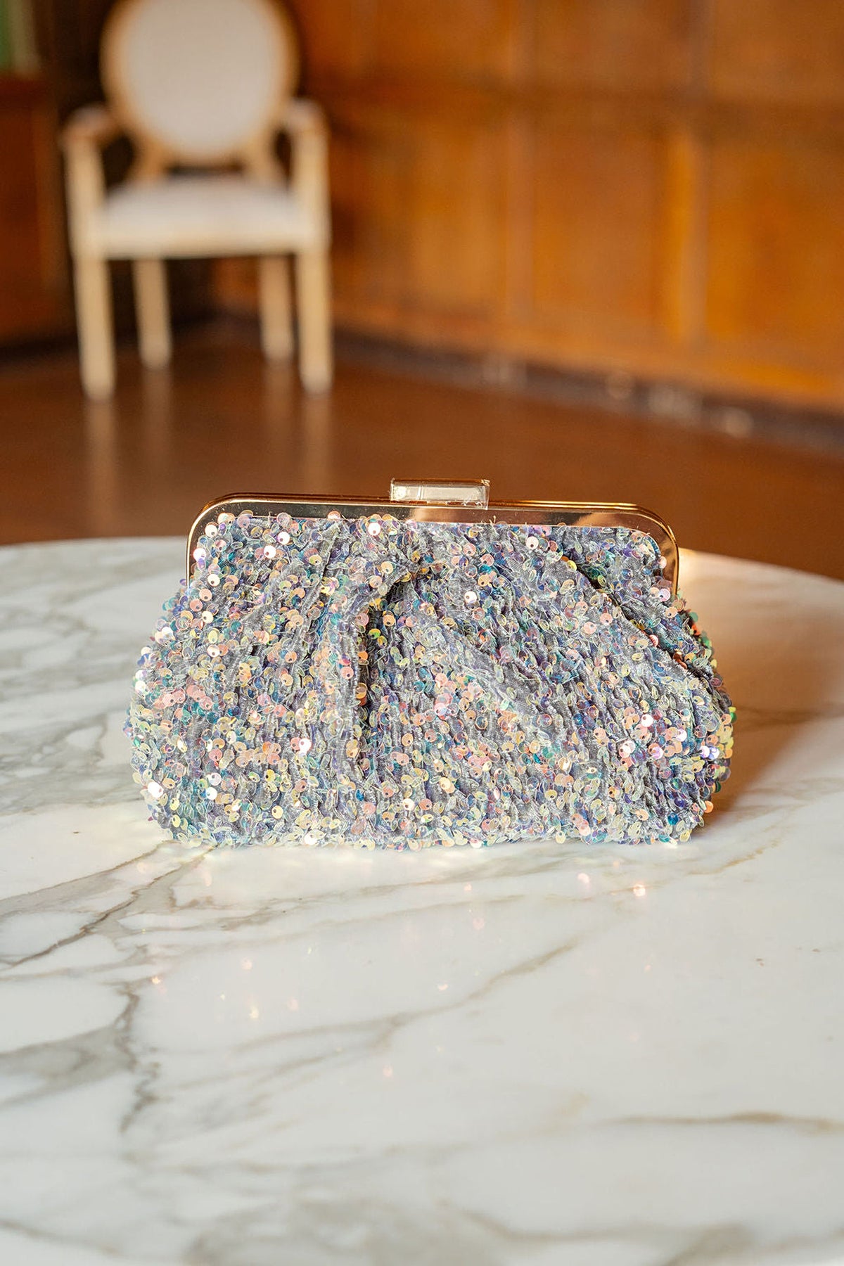 The Trixie sequin clutch with its gold frame on a marble table.