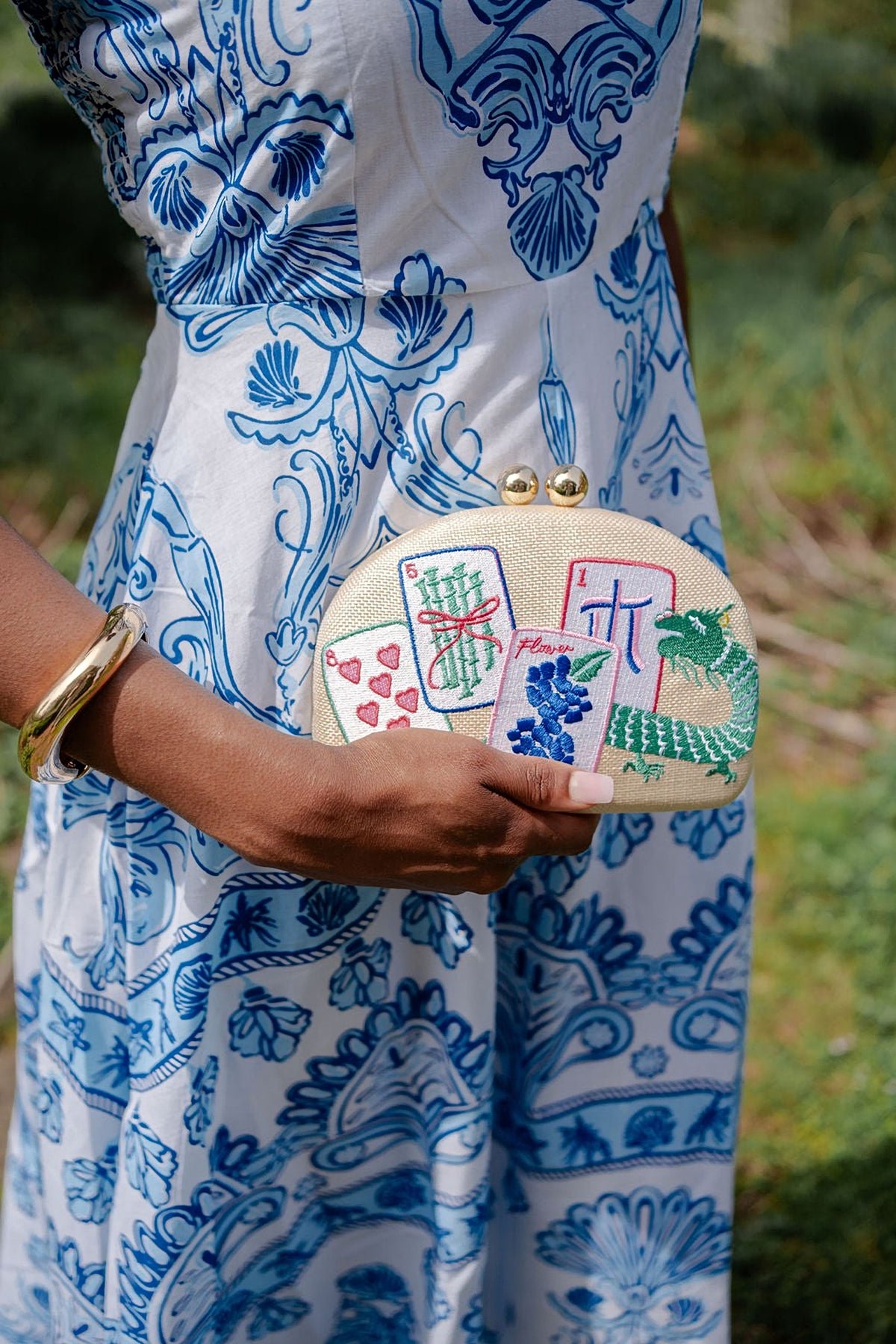 The Mahjong Embroidered Clutch held in one hand against a blue and white printed dress.