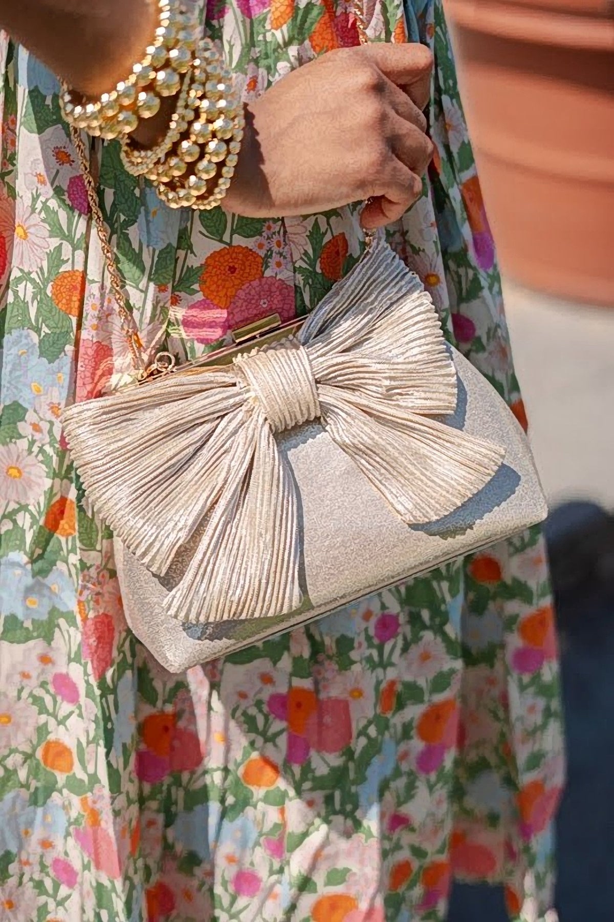The gold Samantha Bag carried on the arm with a floral print dress and pearl bracelets.