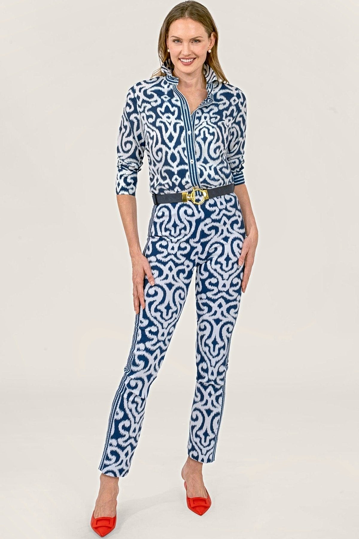 A woman in a matching navy arabesque print shirt and pull-on pants with a black belt and red flats.