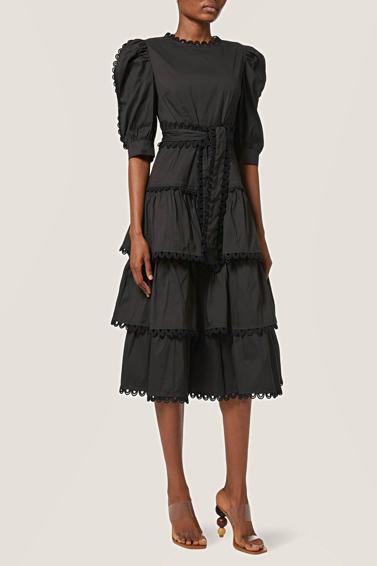 Front view of the black tiered cotton midi dress with puff half sleeves, a tie belt and looped trim.