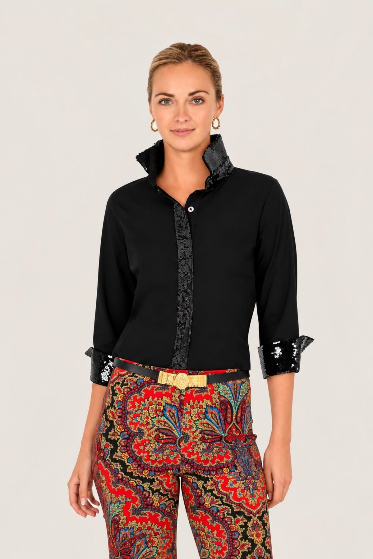 A woman modeling a black long-sleeve button-up shirt with a patterned front placket and black lace-trimmed cuffs, paired with colorful patterned trousers, against a plain light background.