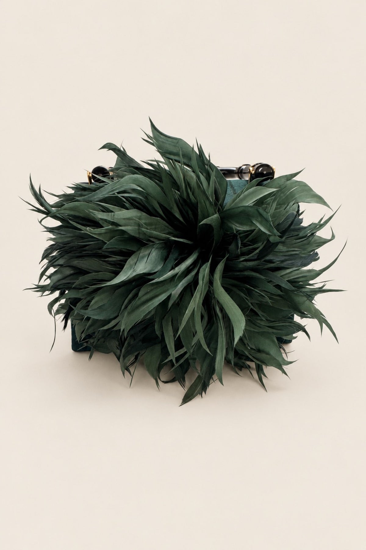 A dark green feathered clutch purse with a structured base and small metallic hardware, photographed on a solid light beige background.