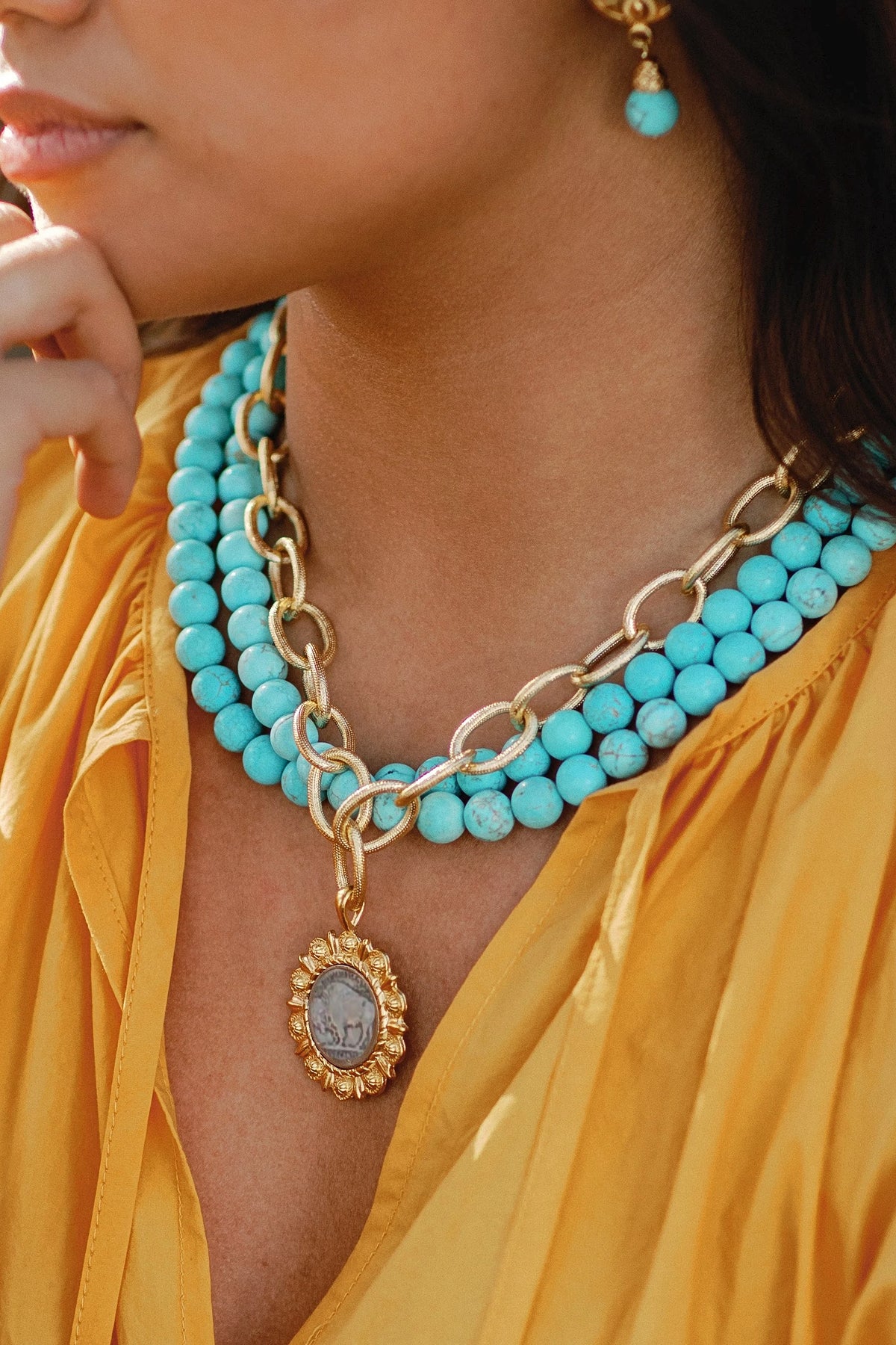Model in a yellow blouse wearing the three-row matte turquoise necklace with a gold Buffalo Nickel pendant.