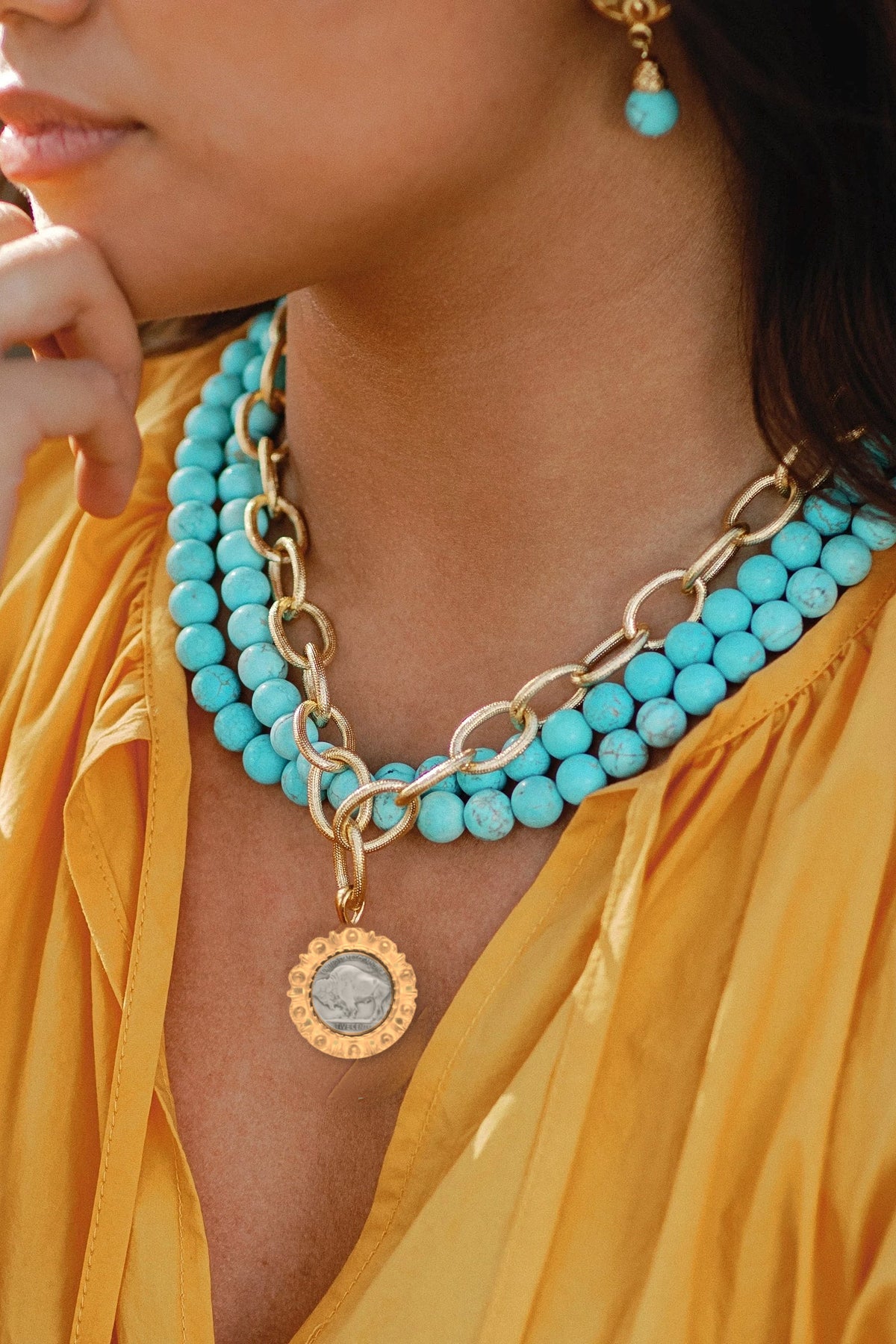 Model in a yellow blouse wearing the three-row matte turquoise necklace with a gold Buffalo Nickel pendant.