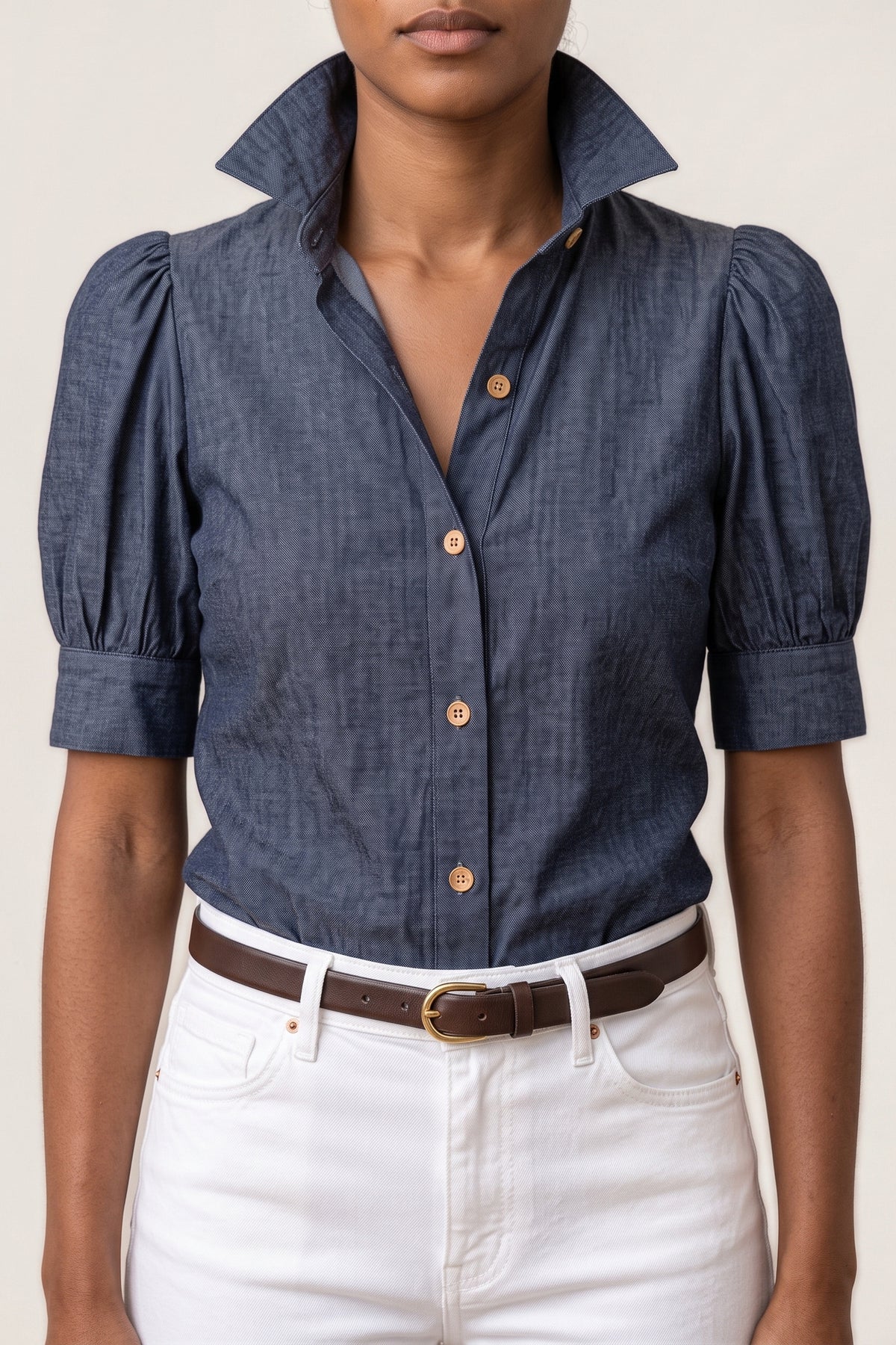 Close-up of the Chambray Puff Sleeve Top showing the tall stand-up collar, the button placket with matte tan buttons and a gathered puff sleeve with its band cuff