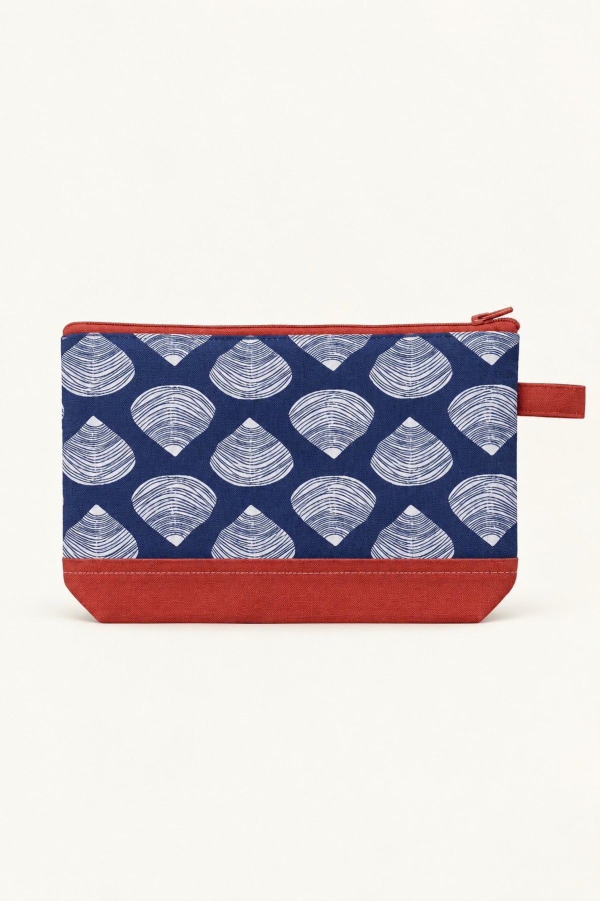 The Clamshell cosmetic bag in navy with white clam shells, a coral bottom and zip, shown from the front.