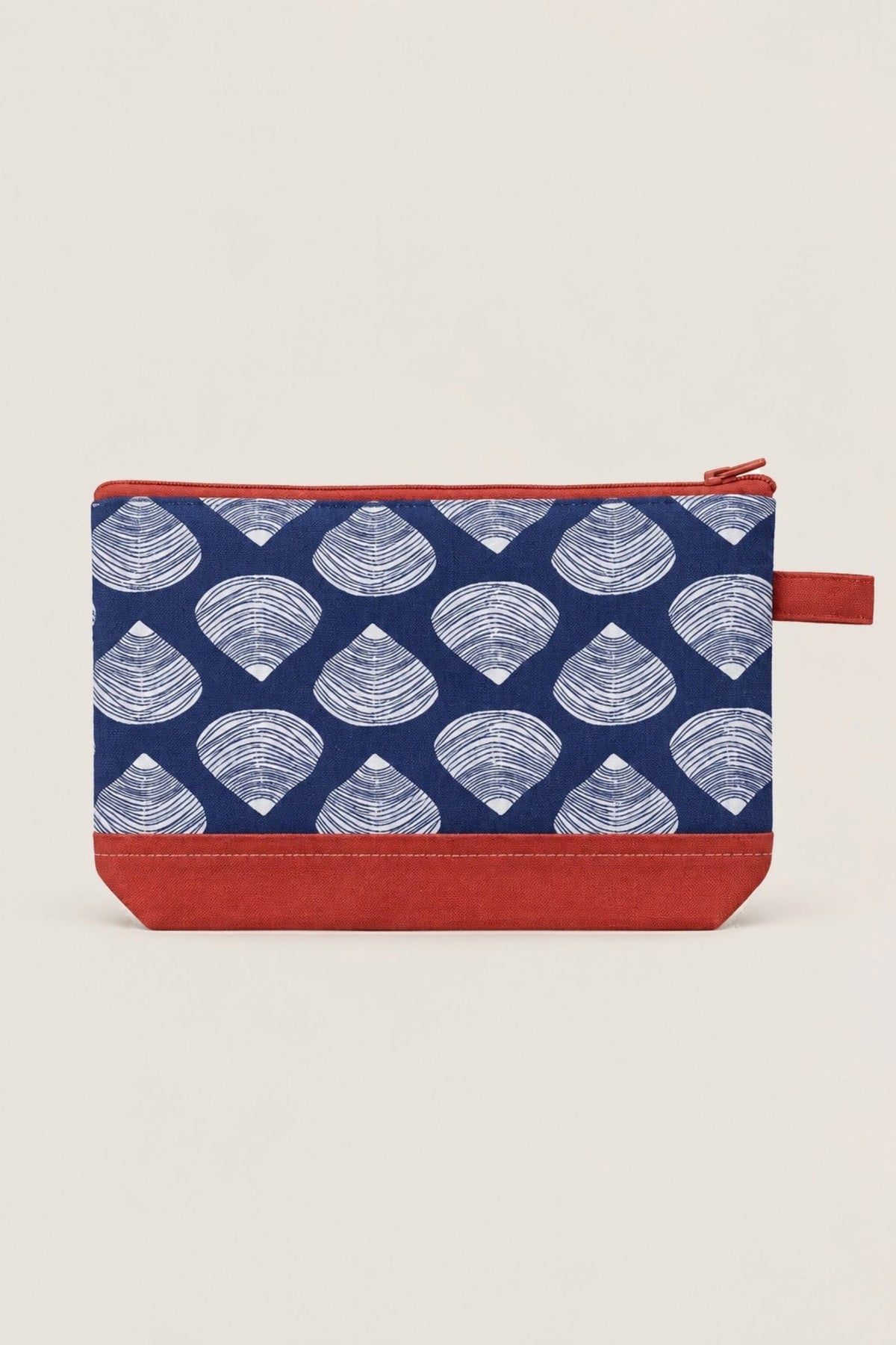 The Clamshell cosmetic bag in navy with white clam shells, a coral bottom and zip, shown from the front.