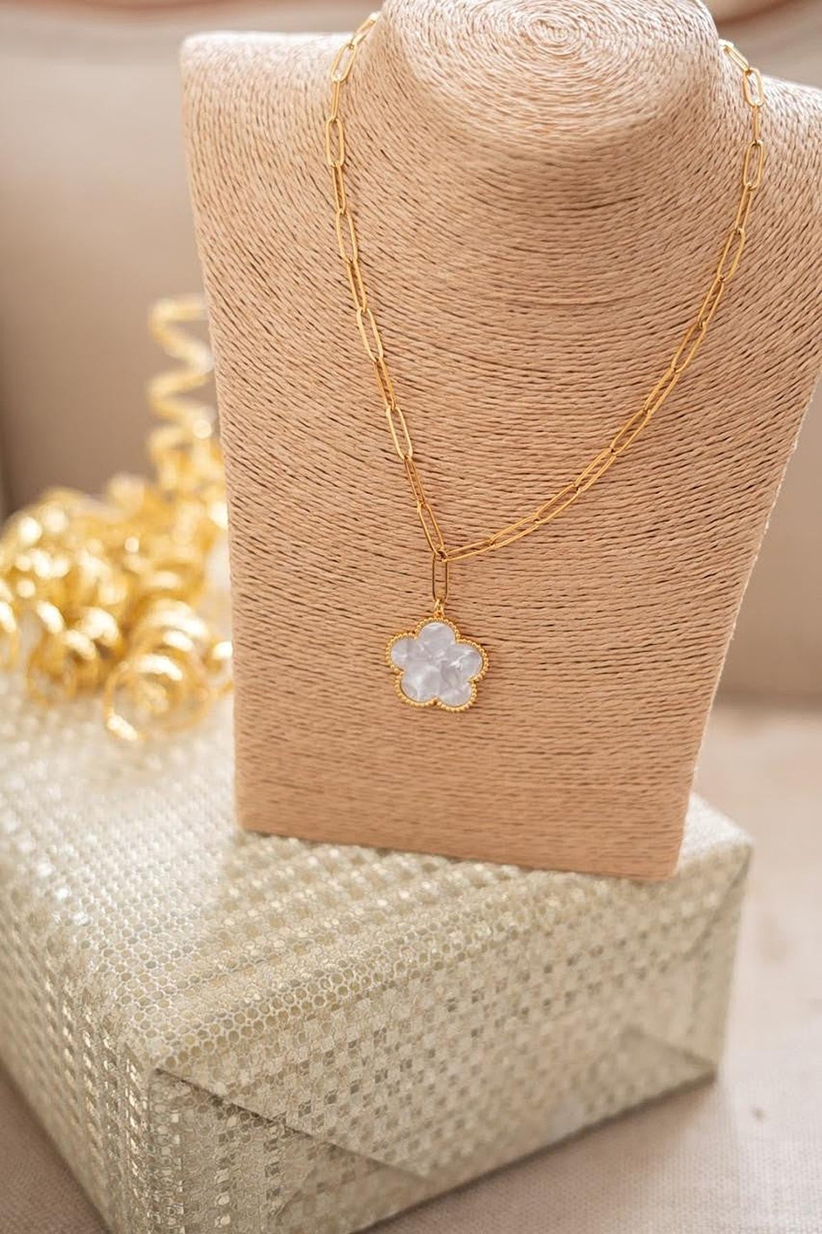Gold Clover Paperclip Necklace with its mother-of-pearl clover pendant, styled on a raffia bust.