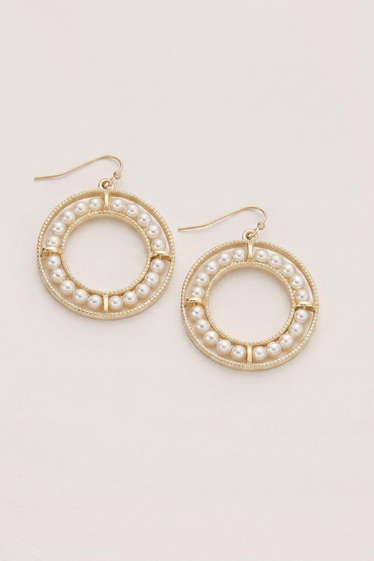 A pair of gold-tone hoop earrings decorated with small white faux pearls, shown on a plain off-white background.