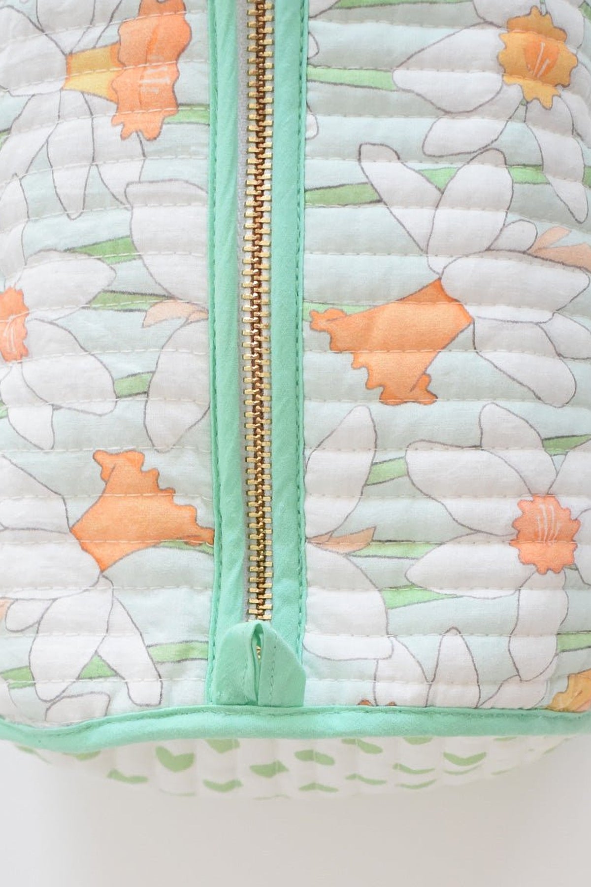 A close-up of the Daffy cosmetic pouch's quilted top with its brass zip and mint piping.