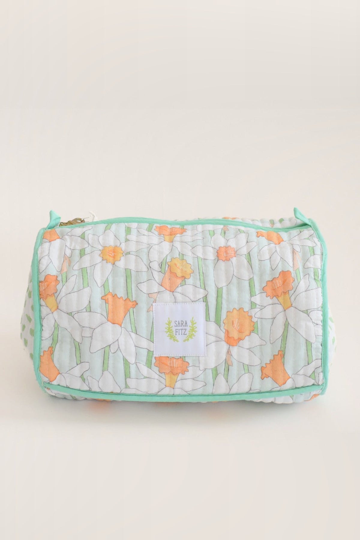 The Daffy quilted cosmetic pouch with white and orange daffodils, mint trim and a Sara Fitz label, shown from the front.