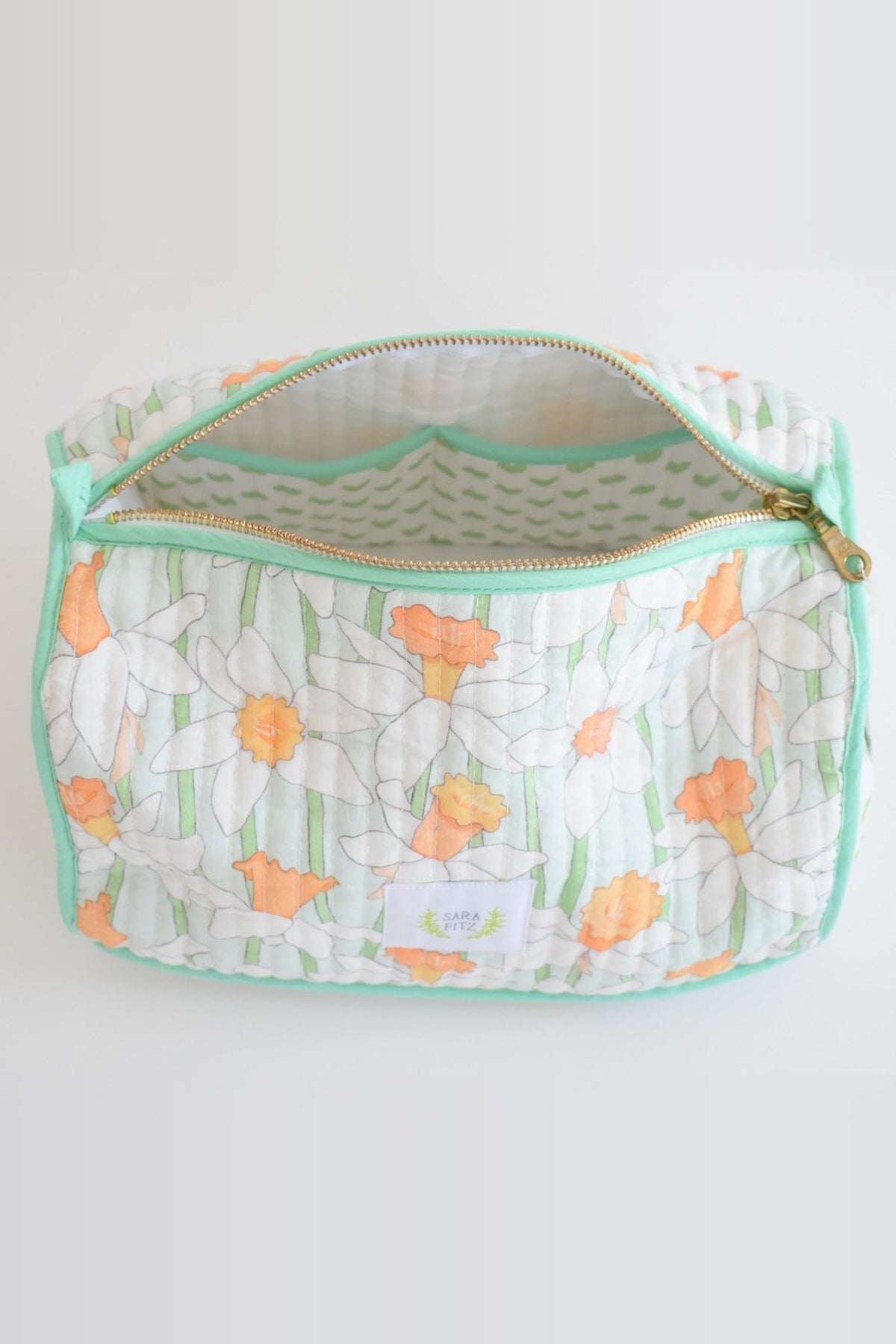 The Daffy cosmetic pouch unzipped, showing its white lining printed with green dashes and the brass zip.