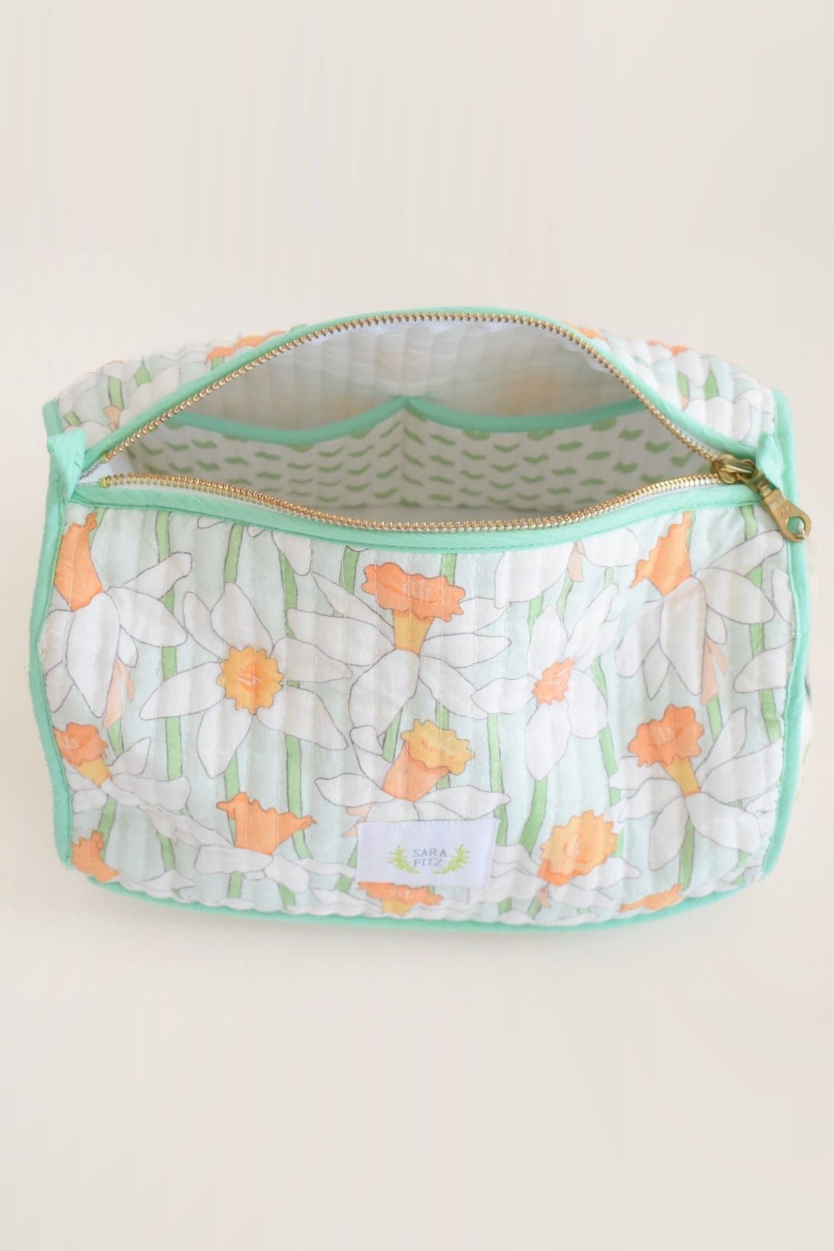 The Daffy cosmetic pouch unzipped, showing its white lining printed with green dashes and the brass zip.