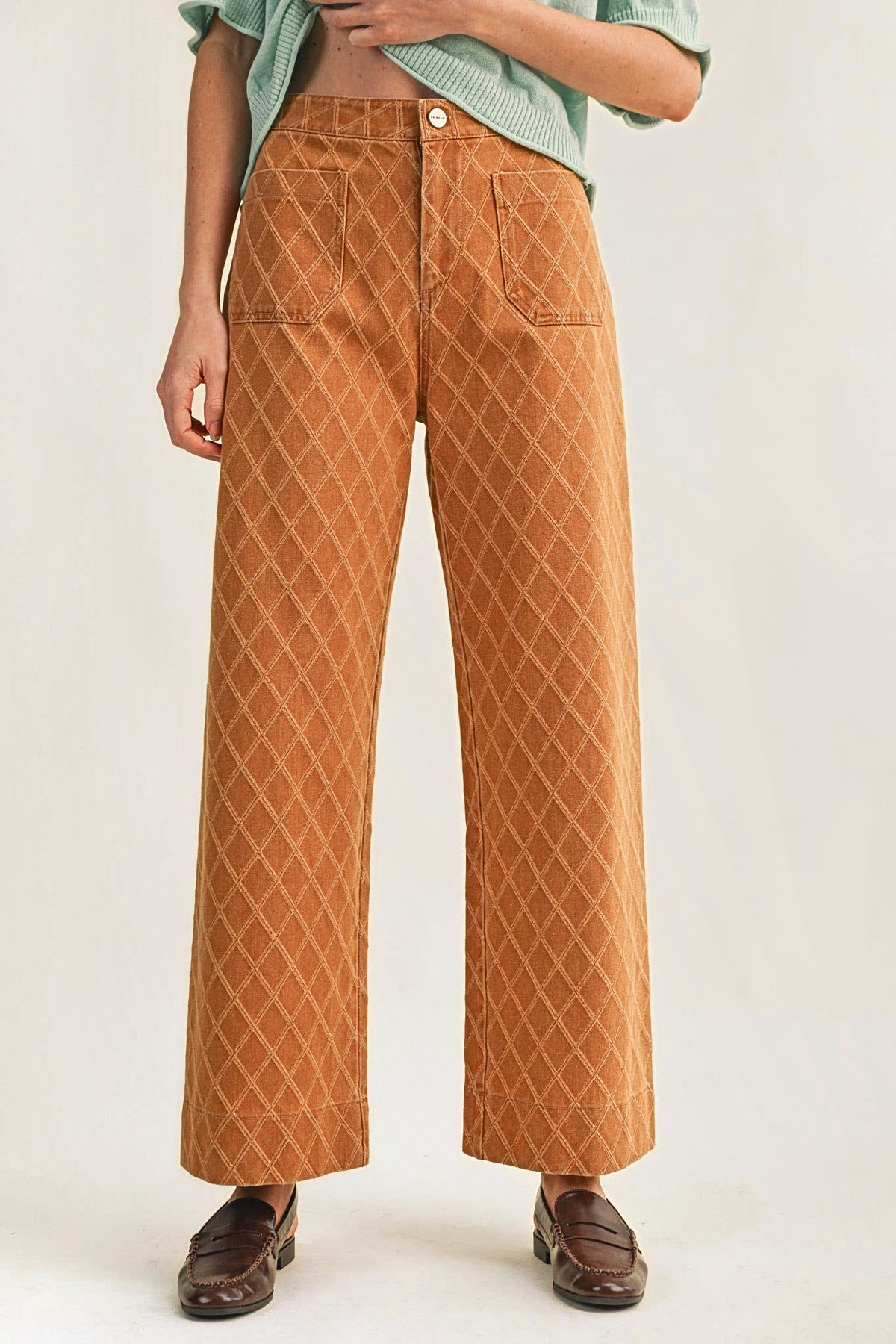 Front view of high-waisted wide-leg pants with a diamond quilted texture, front patch pockets and a button closure, worn with brown loafers.