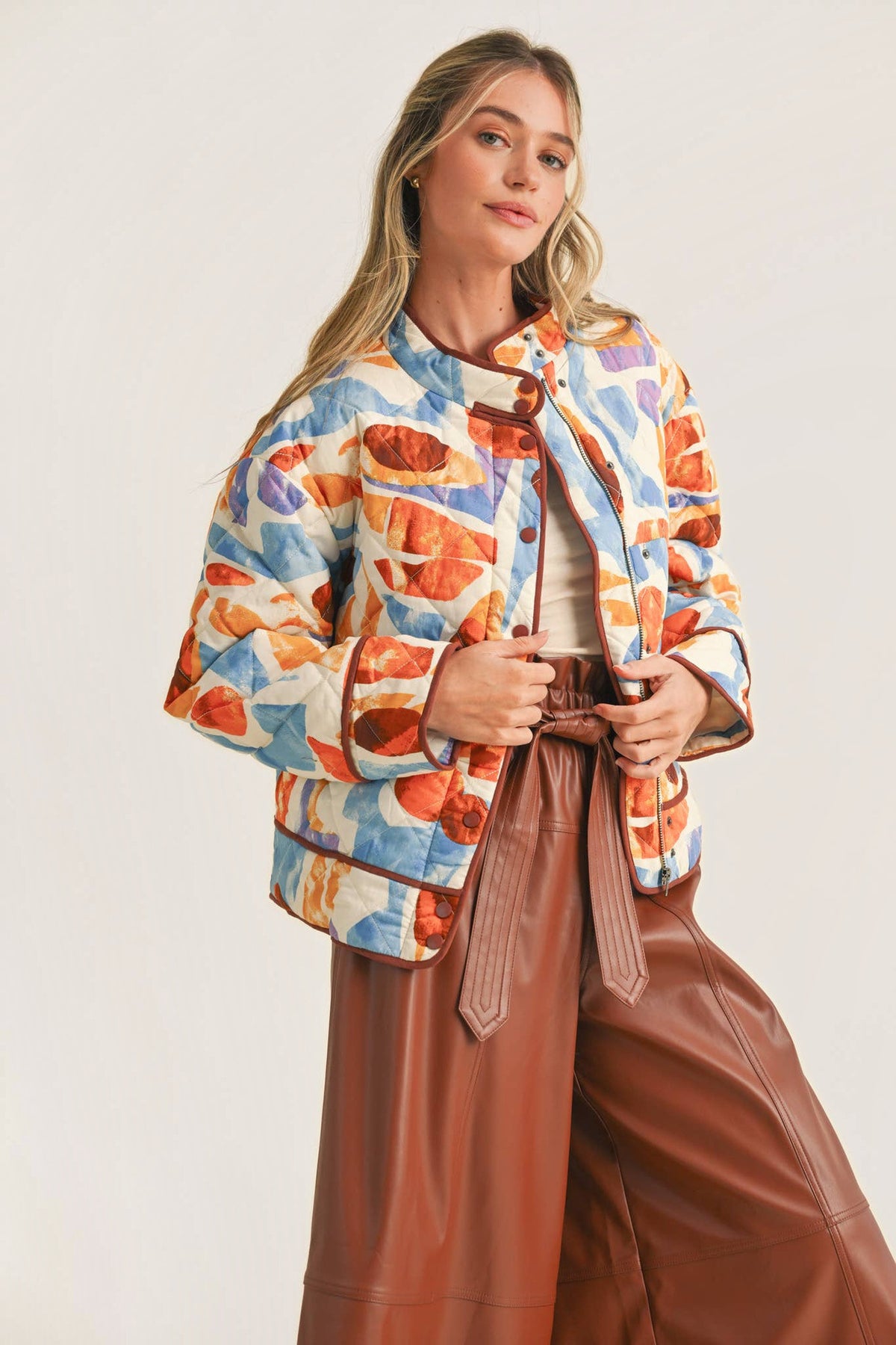 A woman in the Exclusive Print Quilted Jacket, three-quarter view, holding the front of the jacket, showing the watercolor print and contrast binding