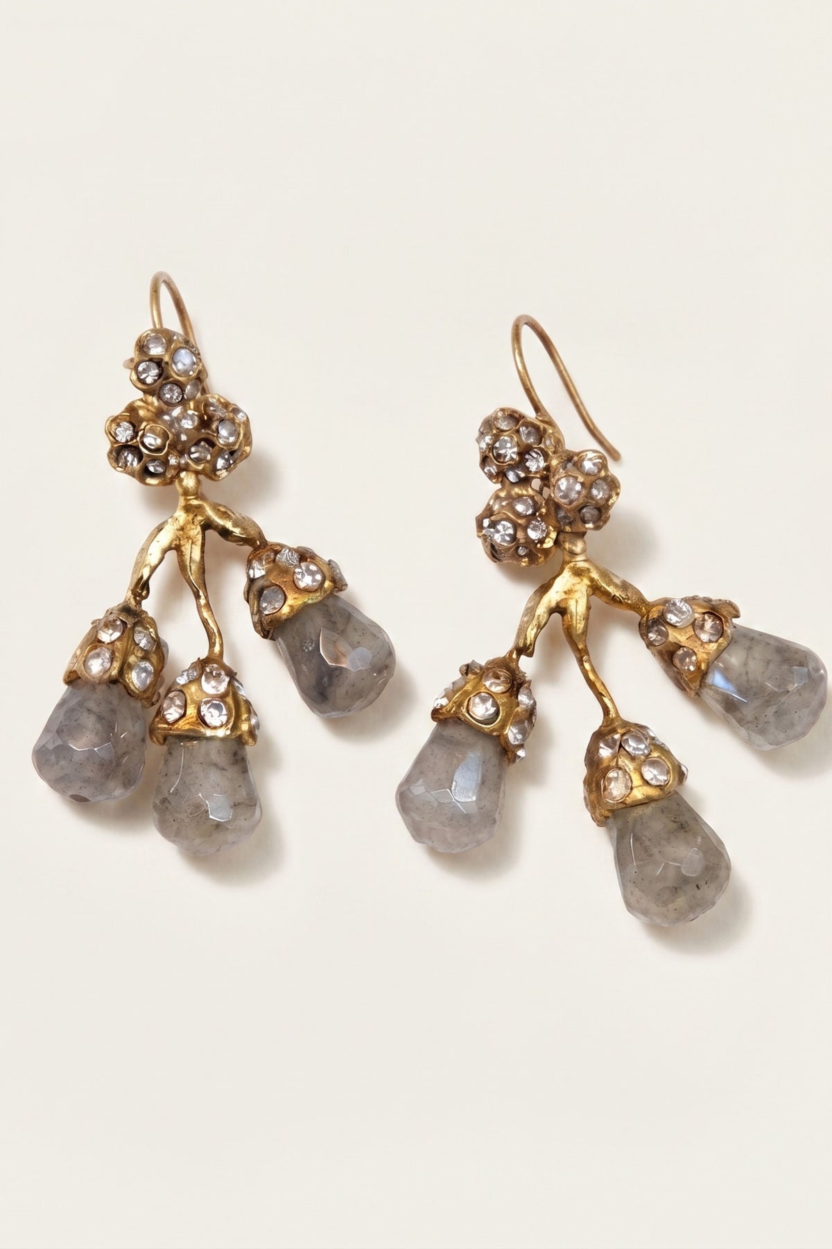 A pair of gold-tone dangle earrings with clustered rhinestone details and three teardrop-shaped gray gemstones on each earring, shown on a light cream background.