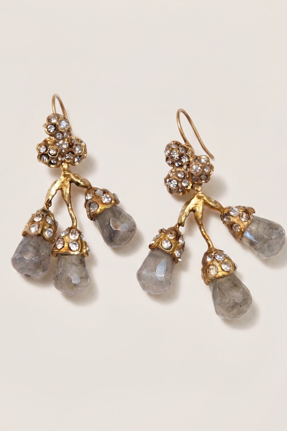 A pair of gold-tone dangle earrings with clustered rhinestone details and three teardrop-shaped gray gemstones on each earring, shown on a light cream background.
