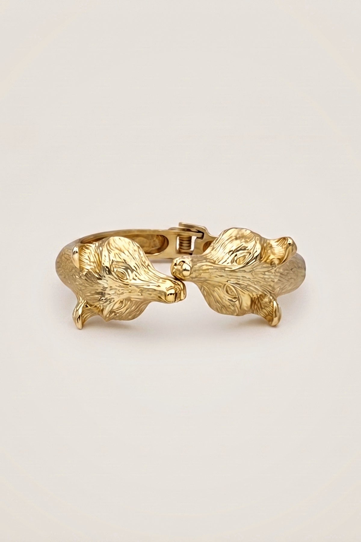 Golden Fox Hinged Bracelet, a gold-tone bangle with two sculpted fox heads meeting at the front, on a warm greige backdrop.