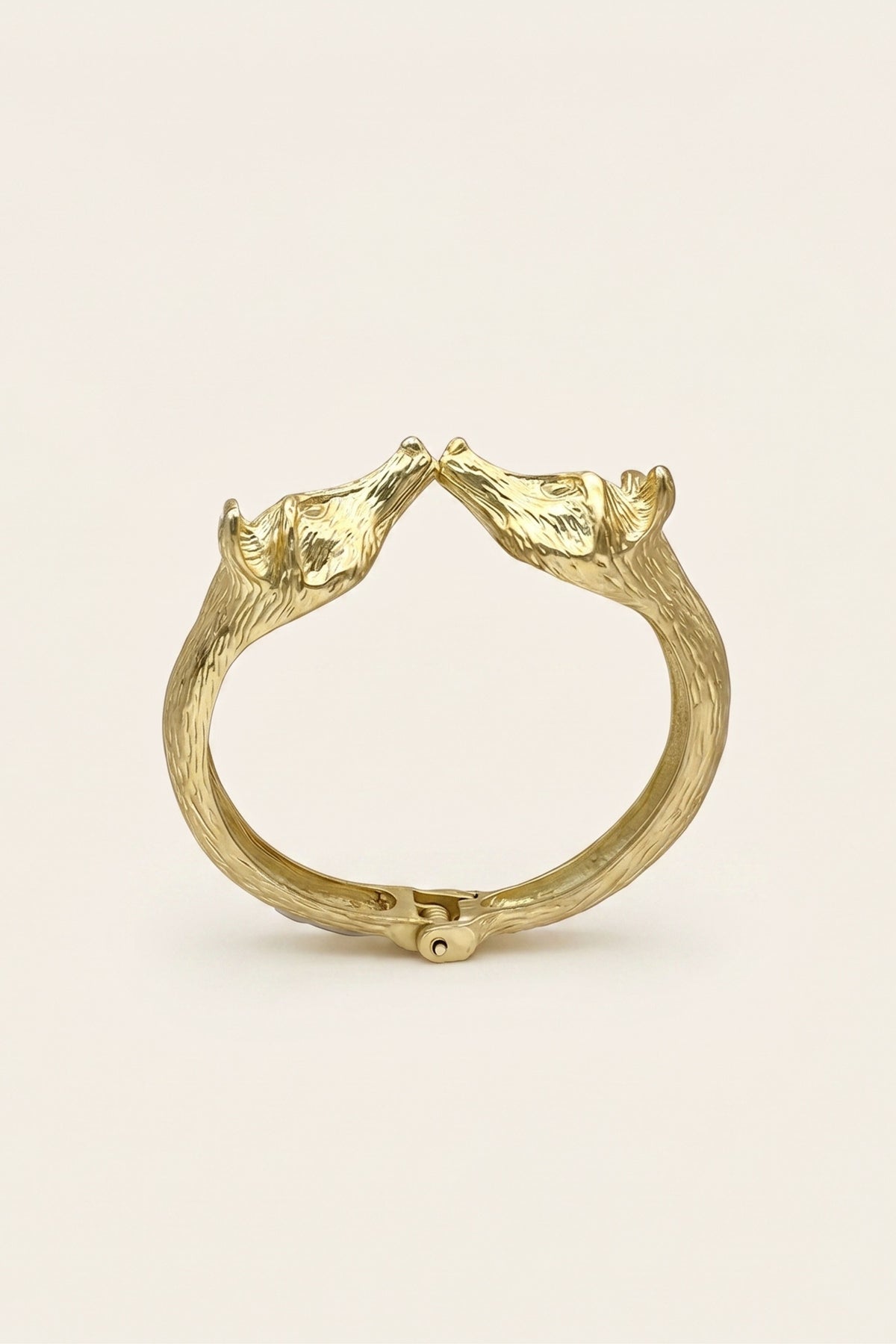 A gold-toned metal ring featuring two sculpted fox heads facing inward at the top, photographed on a clean, solid off-white background.