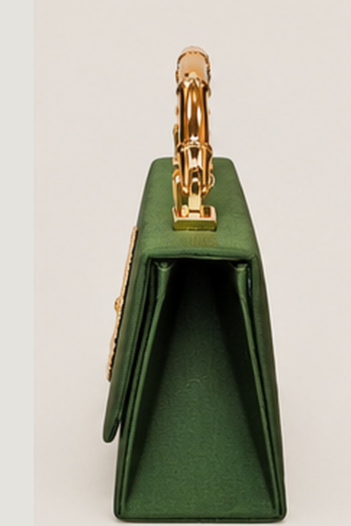 A structured green handbag shown from a side profile view, featuring a prominent gold-tone handle and gold hardware details, set against a plain light gray background.