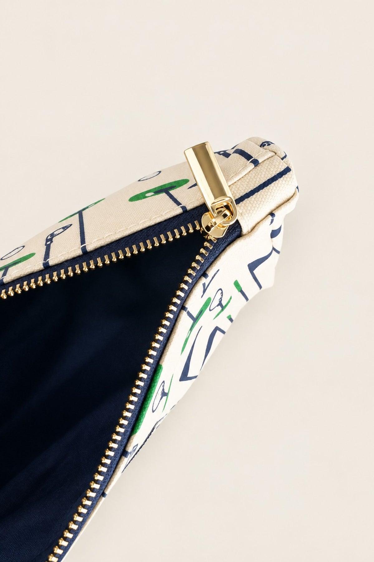 Close-up of a zippered pouch with a cream and navy graphic print, a gold-tone zipper pull, and a dark navy interior lining, set against a solid light beige background.