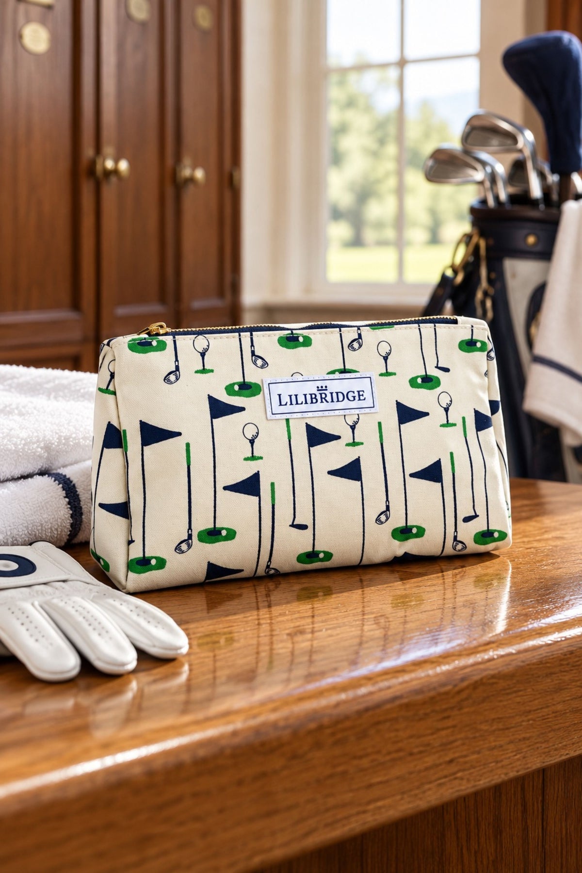 A zippered cosmetic pouch with a golf-themed print of flags, clubs, and tees, featuring a 'LILIRIDGE' label, displayed on a wooden table with golf props in a warm indoor setting.