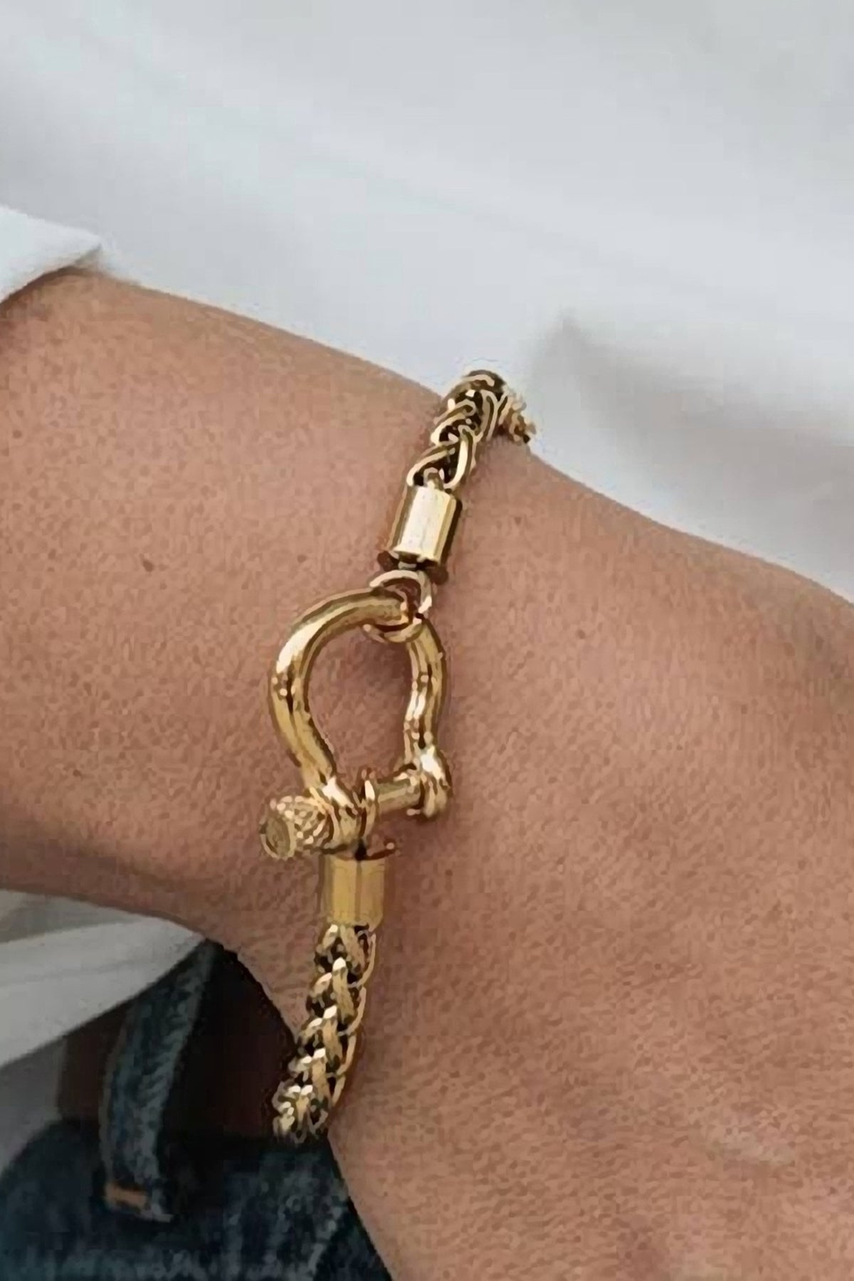 The gold Horse Bit carabiner charm bracelet on the wrist with a white shirt sleeve.