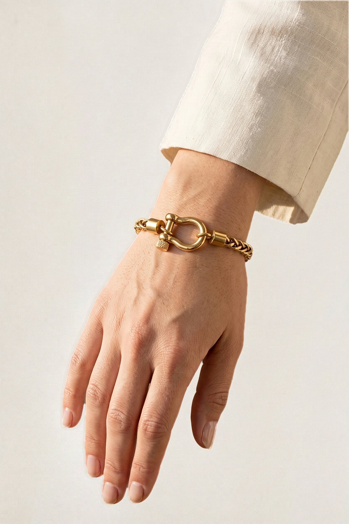 Horse Bit Carabiner Charm Bracelet worn on the wrist with a cream linen sleeve, showing the gold horse bit shackle and wheat chain.