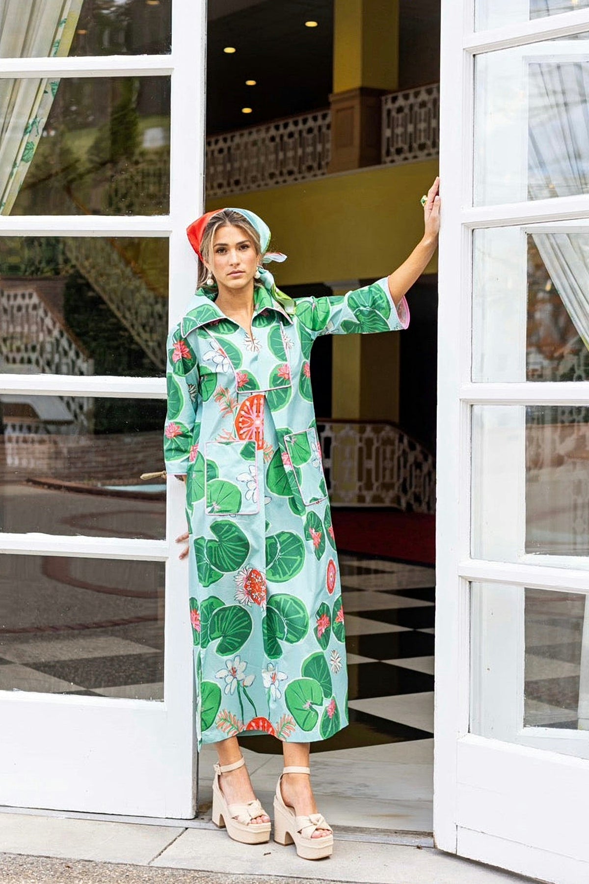 The Lolli Cassidy long dress worn with a head scarf, in a garden doorway.