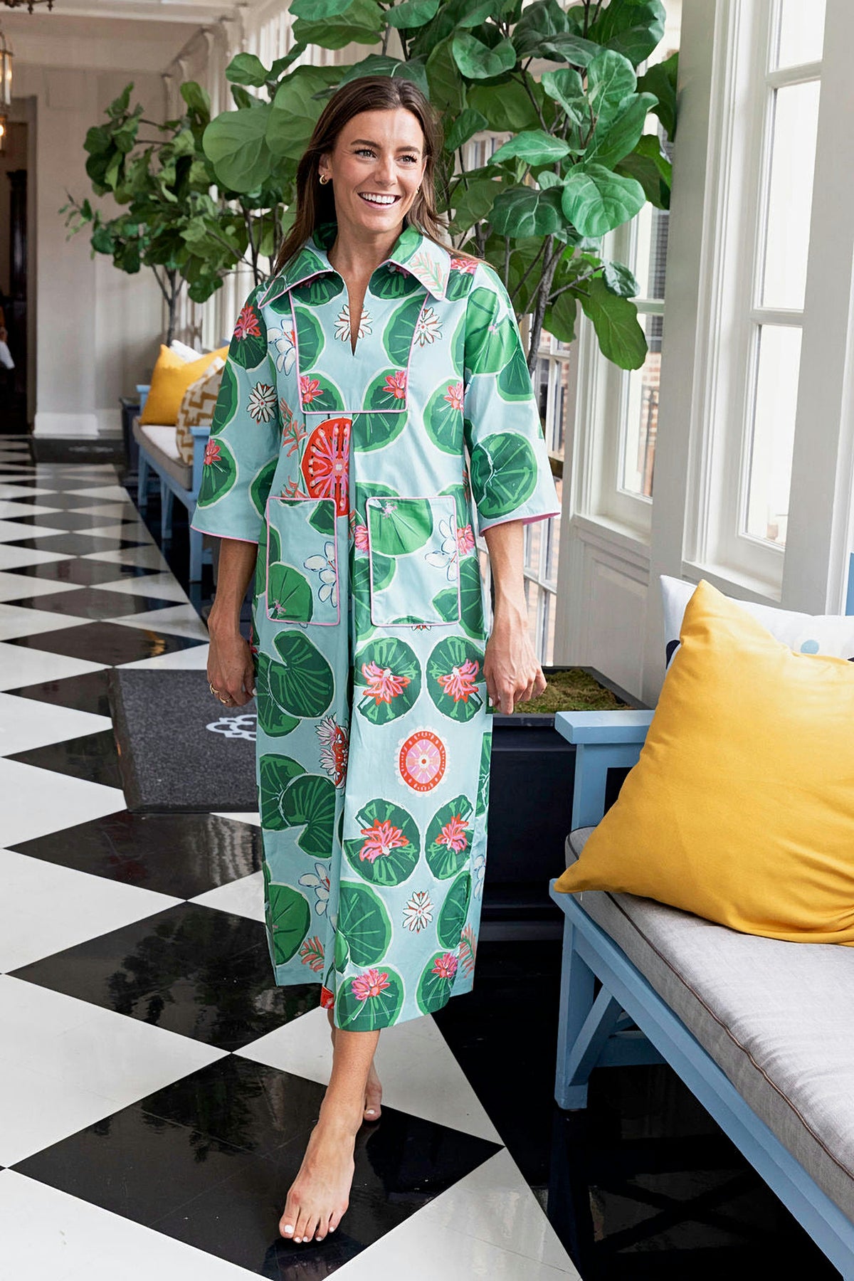 A woman in the Lolli Cassidy long dress with a lily pad print, standing on a black and white checkered floor.