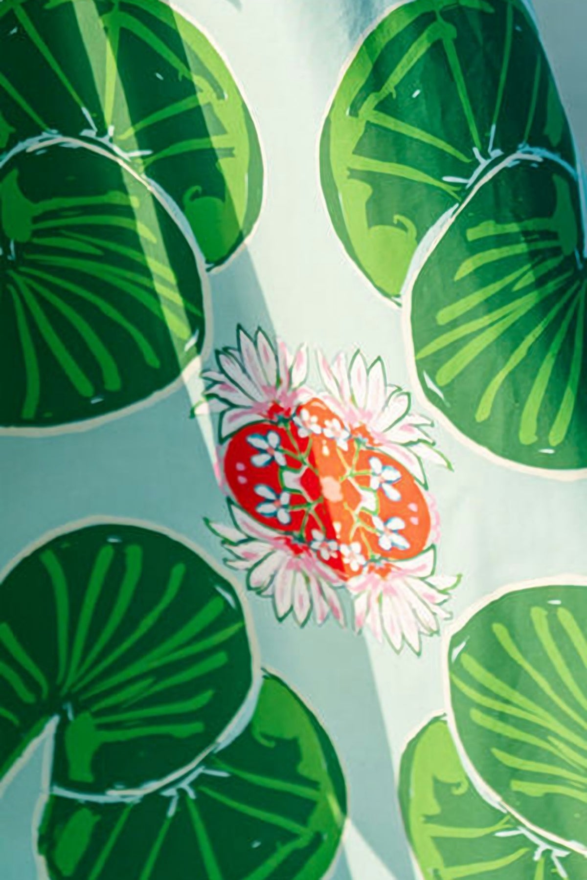 Close-up of the Lolli print: green lily pads and a coral water lily on a soft aqua cotton.