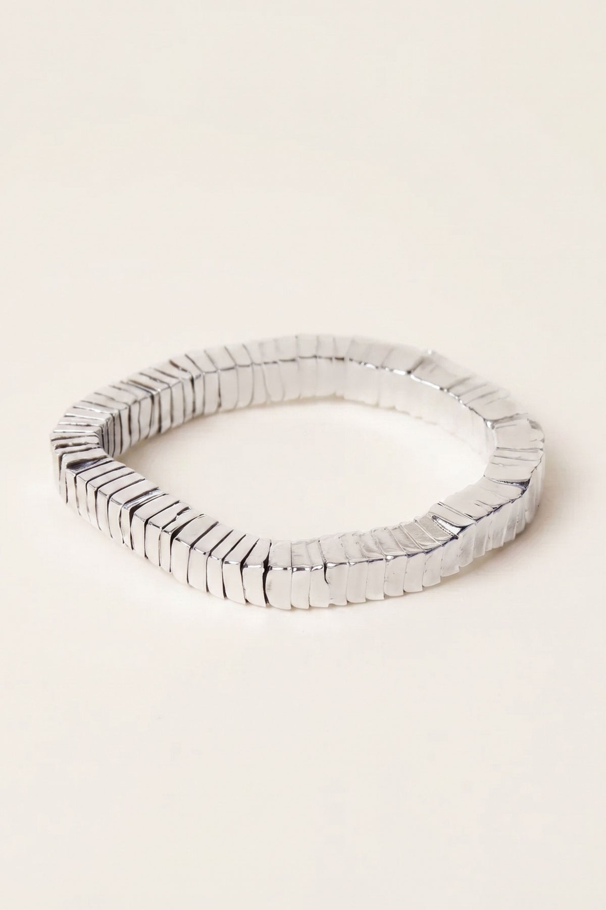 A silver metallic segmented bangle bracelet with a textured, ridged outer surface, displayed on a clean, solid off-white background.