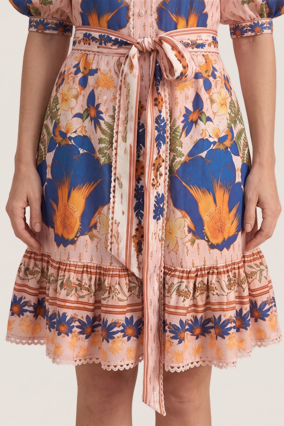 Close-up of the Marseille Garden Dress skirt showing the tie belt tails and the ruffled border-print hem with lace edge