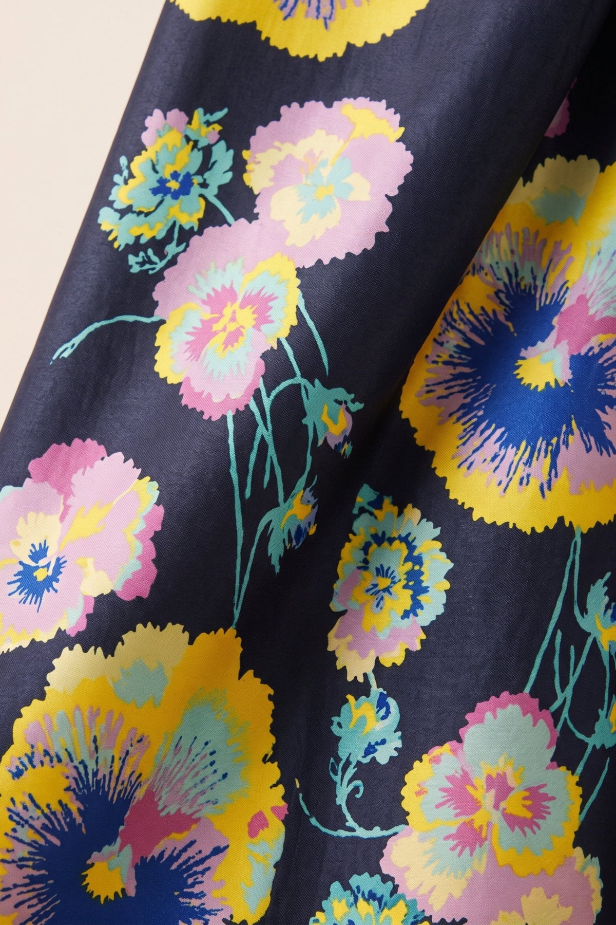 A close-up of a dark fabric with a vibrant, multicolored floral print featuring pink, yellow, and blue flowers with teal stems.