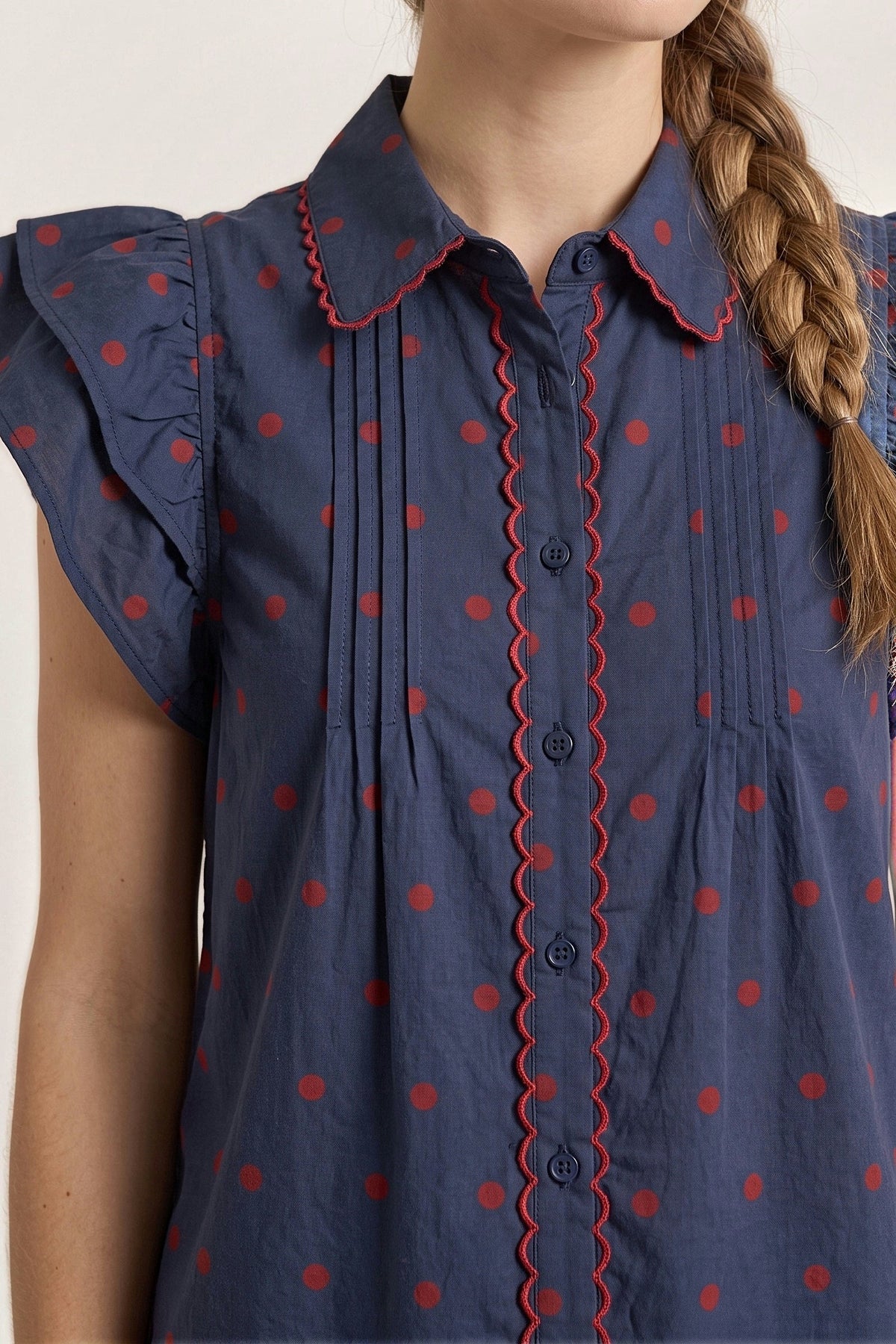 Close-up of the red scalloped collar, placket trim and pintucks on the navy polka dot blouse.
