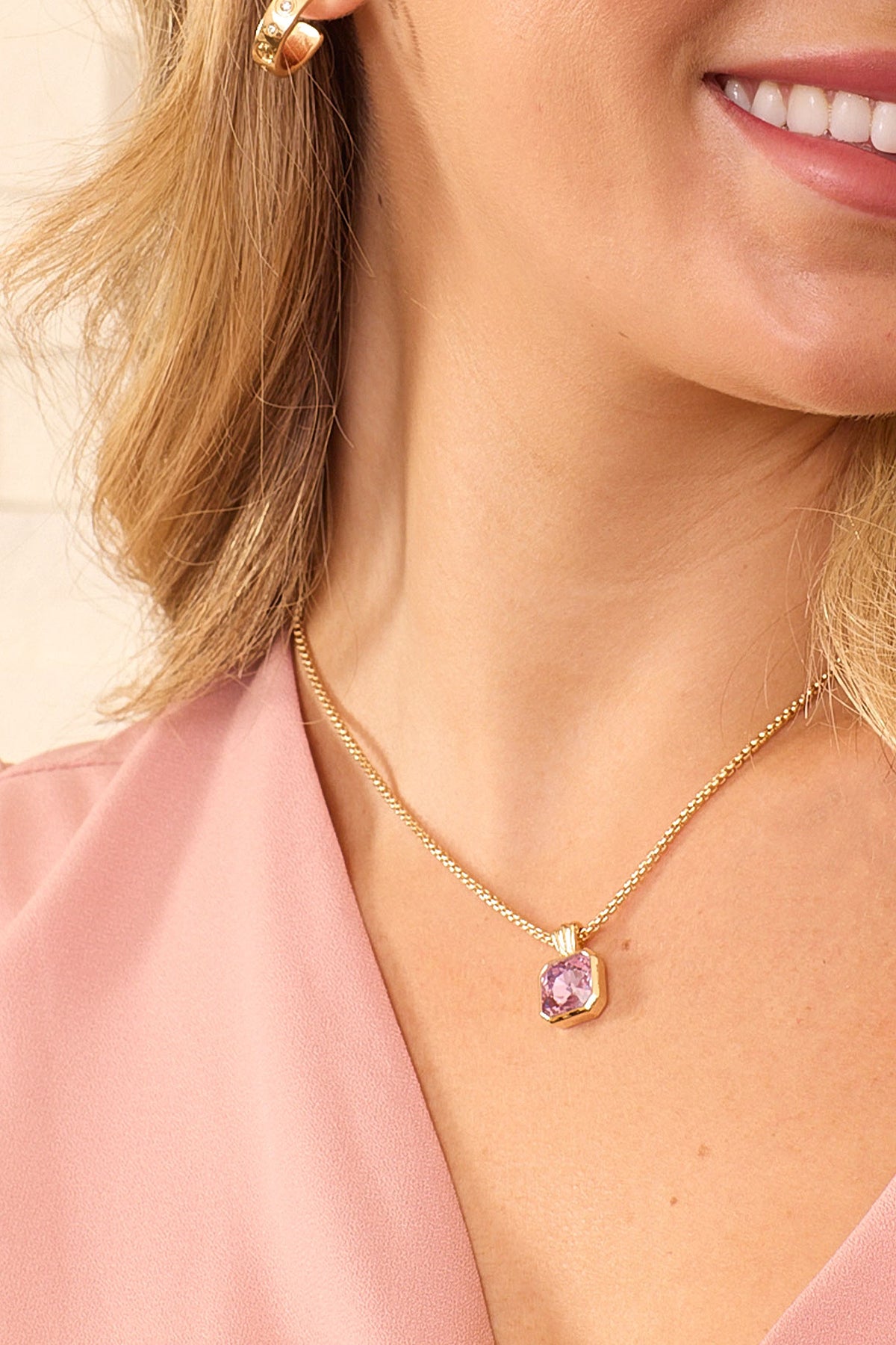 Close-up of a model wearing the gold Orchid Necklace with its lavender crystal pendant resting below the collarbone.