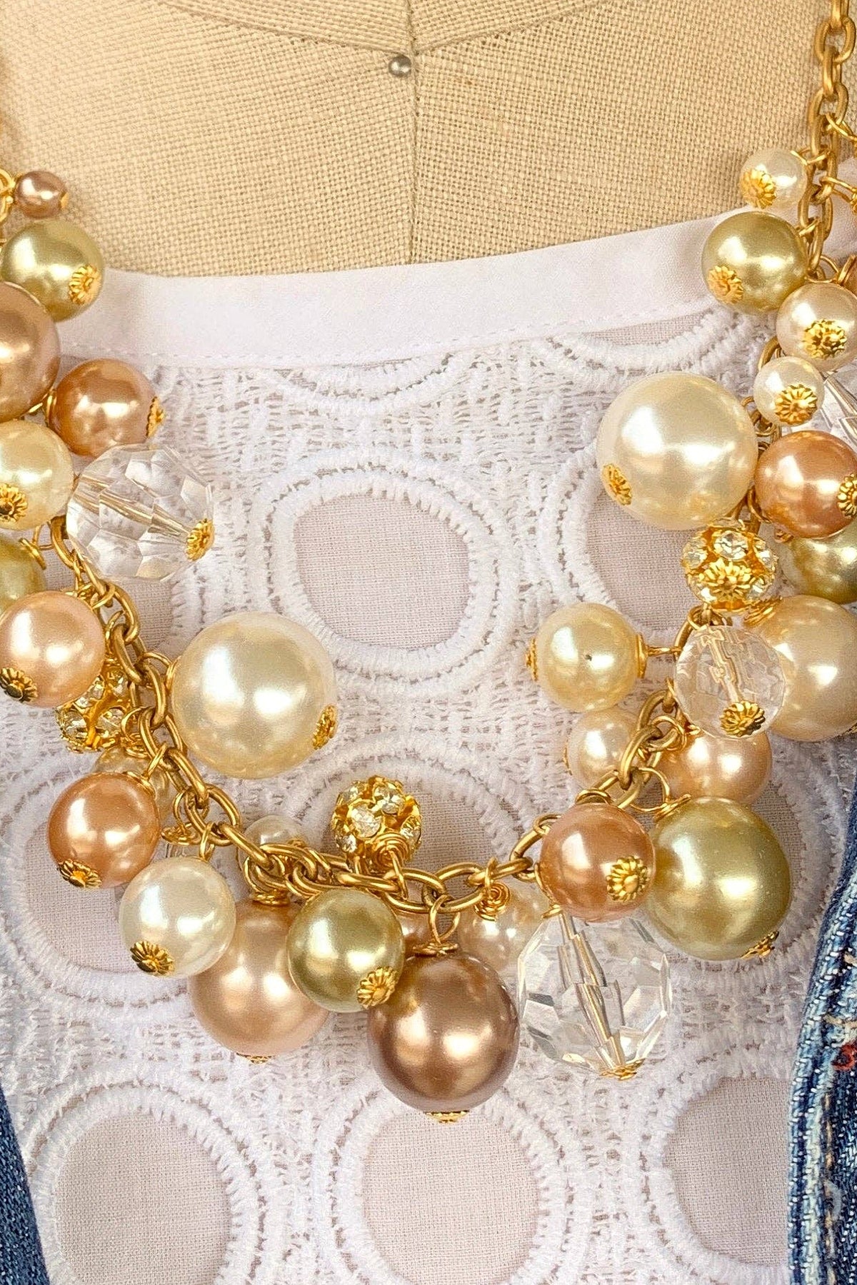 Close-up of the Pearl Charm Necklace showing clusters of champagne, bronze and ivory pearls with faceted crystals and gold caps on a gold chain.