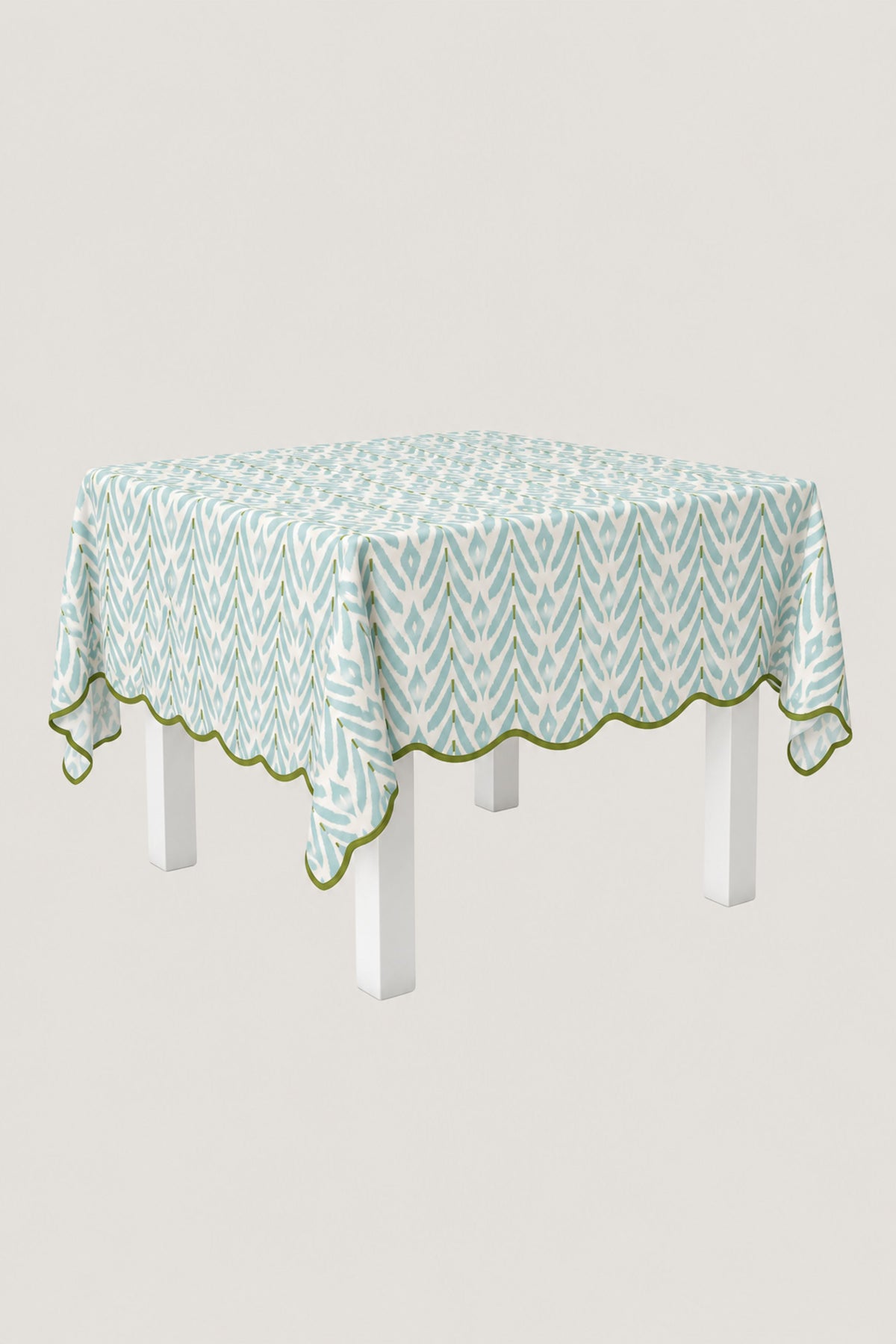A square tablecloth with a light blue and white geometric pattern and a scalloped edge, draped over a white table against a light gray background.