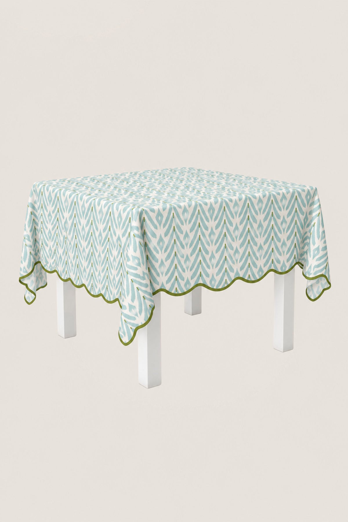 A square tablecloth with a light blue and white geometric pattern and a scalloped edge, draped over a white table against a light gray background.