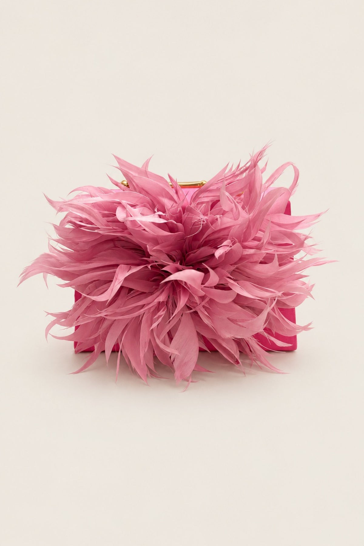 A pink feathered clutch bag with a structured rectangular base and a gold-tone clasp, photographed on a plain light beige background.