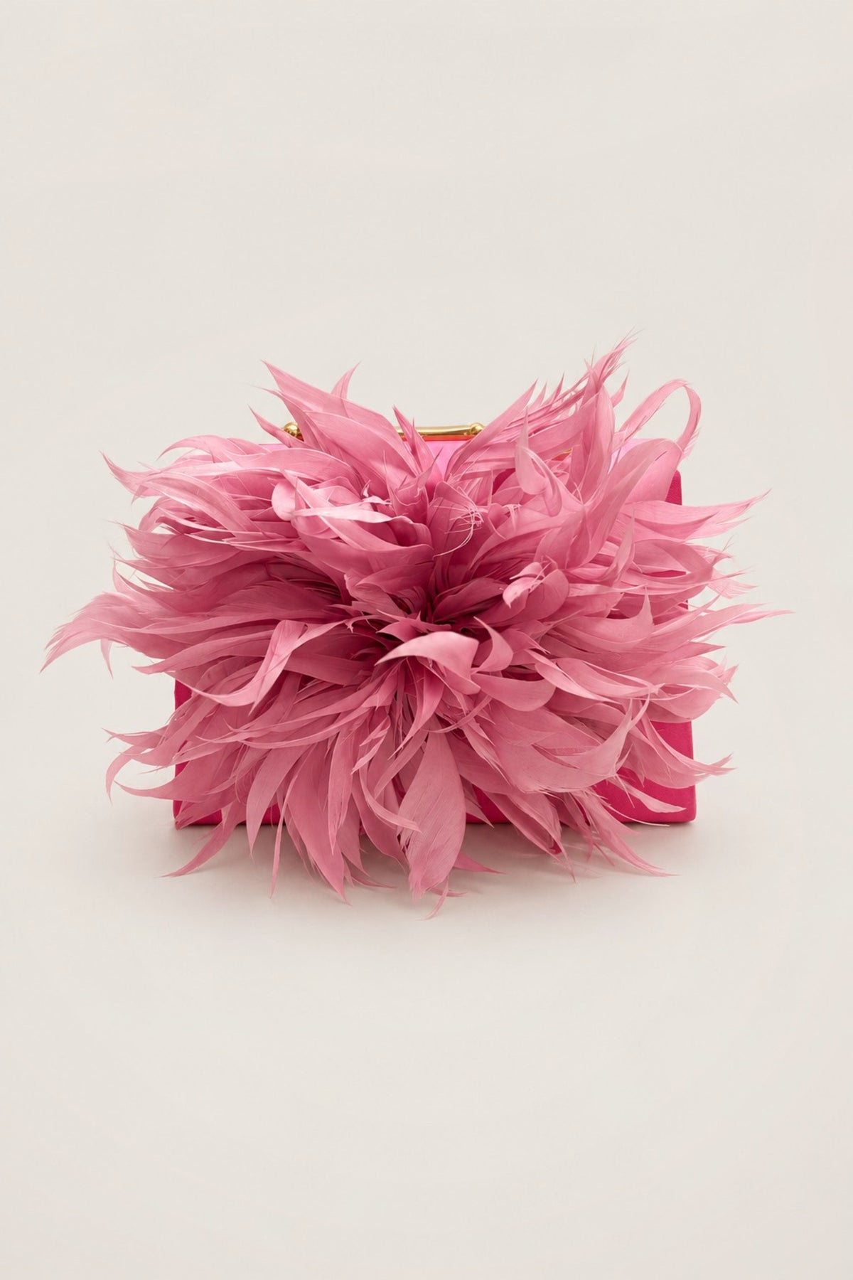 A pink feathered clutch bag with a structured rectangular base and a gold-tone clasp, photographed on a plain light beige background.