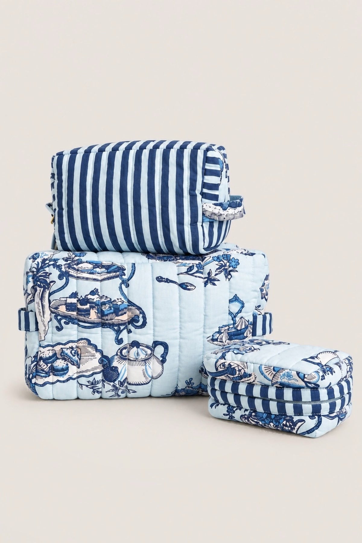 The Three's Best pouch set in blue High Tea toile and navy stripe, three quilted pouches stacked on a white counter.