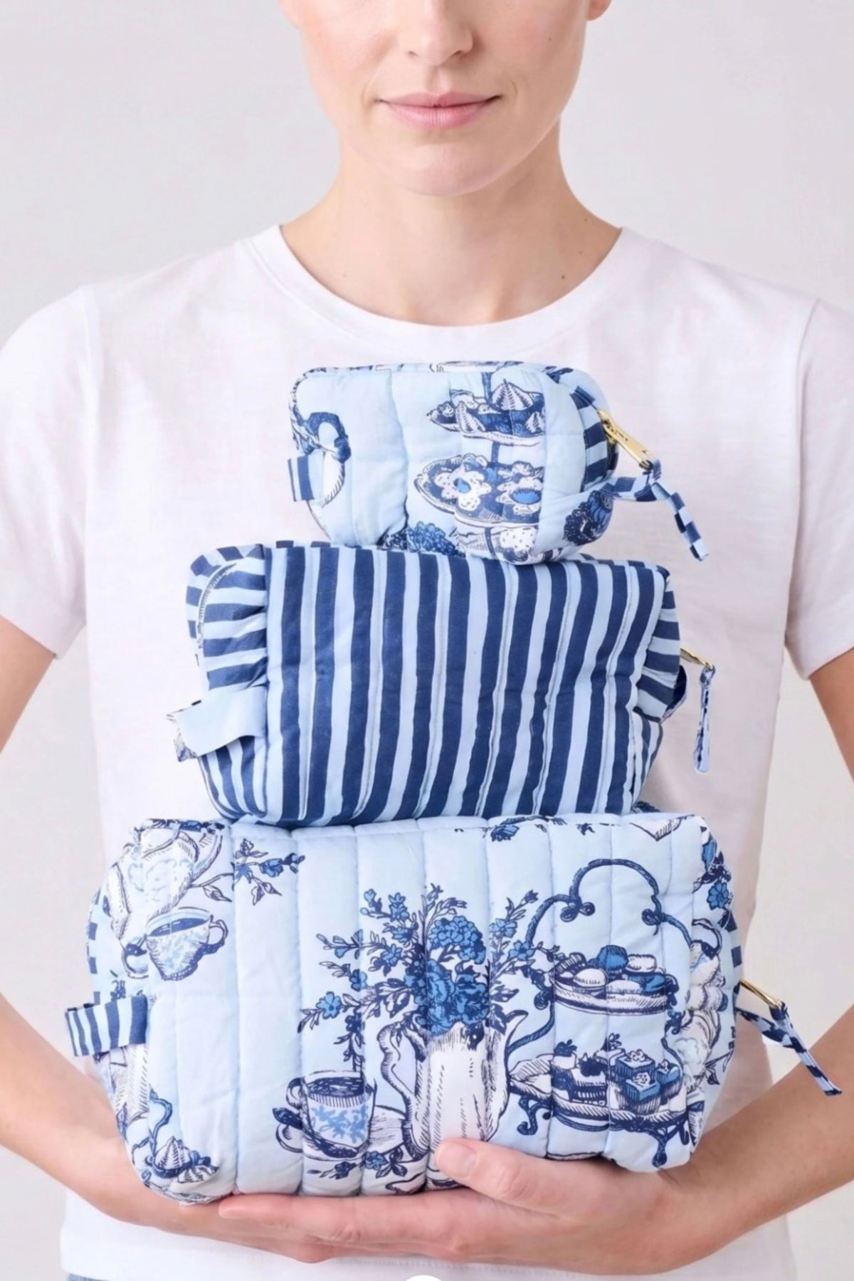 A woman in a white T-shirt holding the three High Tea toile pouches stacked in her hands.