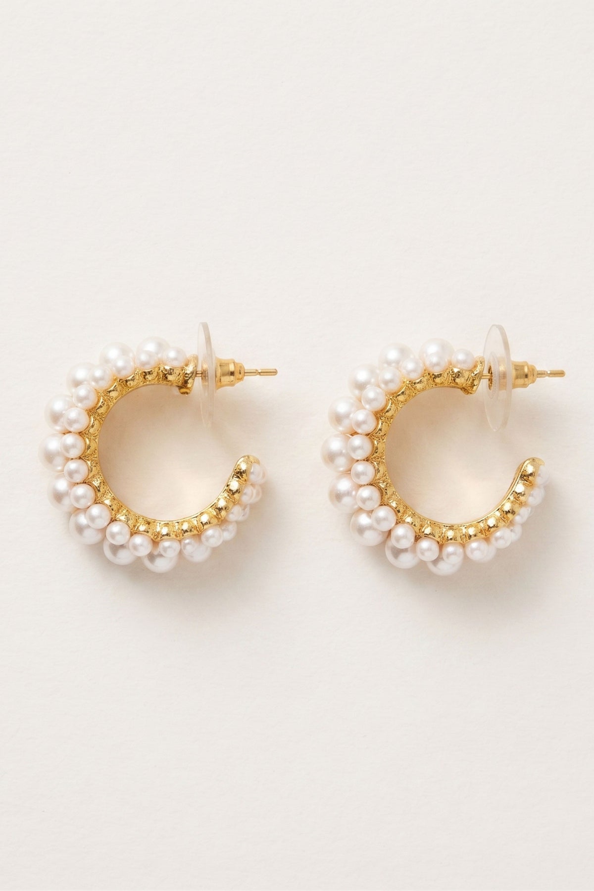 Gold hoop earrings adorned with rows of small white pearls, shown on a plain off-white background.