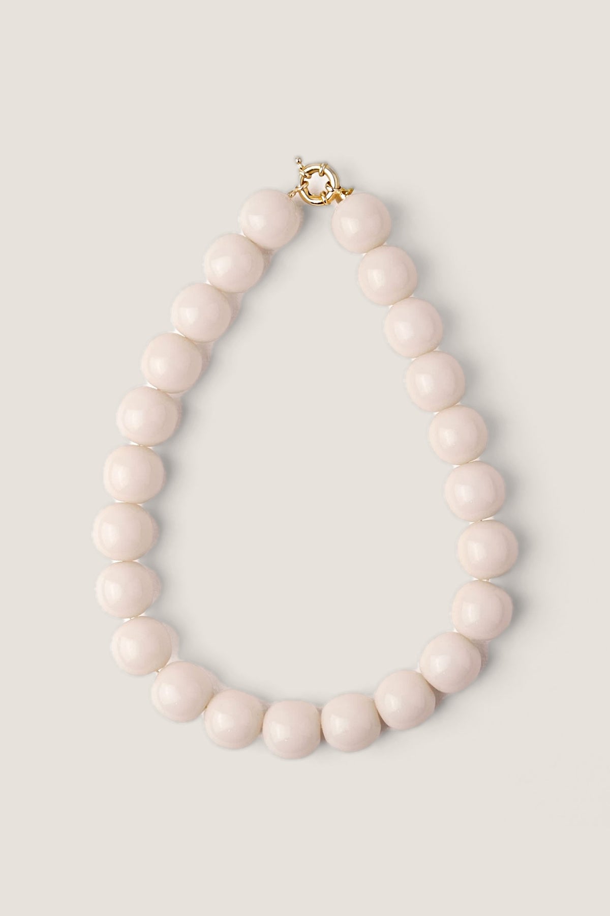 The White Iris large resin bead necklace in milky white laid in an oval on a warm greige backdrop, gold spring-ring clasp at the top.