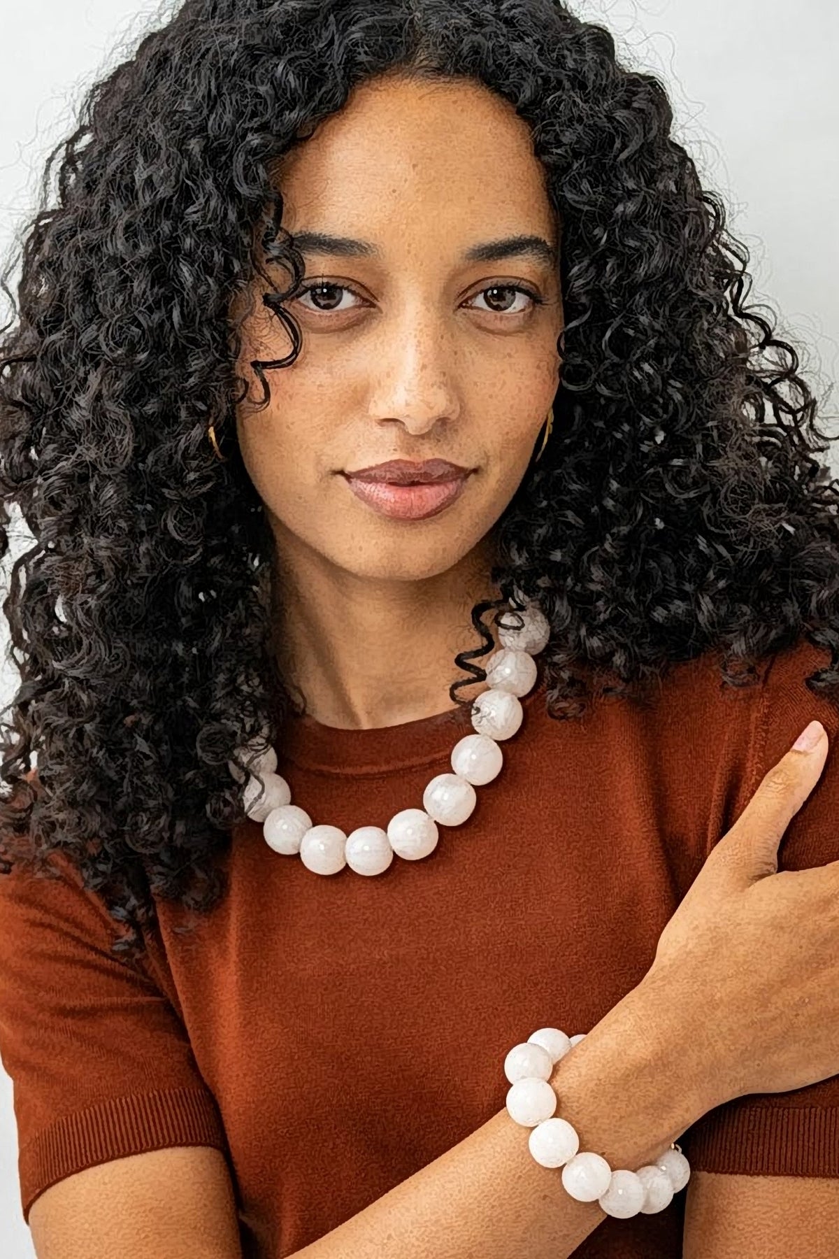Model in a rust knit top wearing the milky white Iris resin bead necklace at the collarbone, with the matching bracelet.