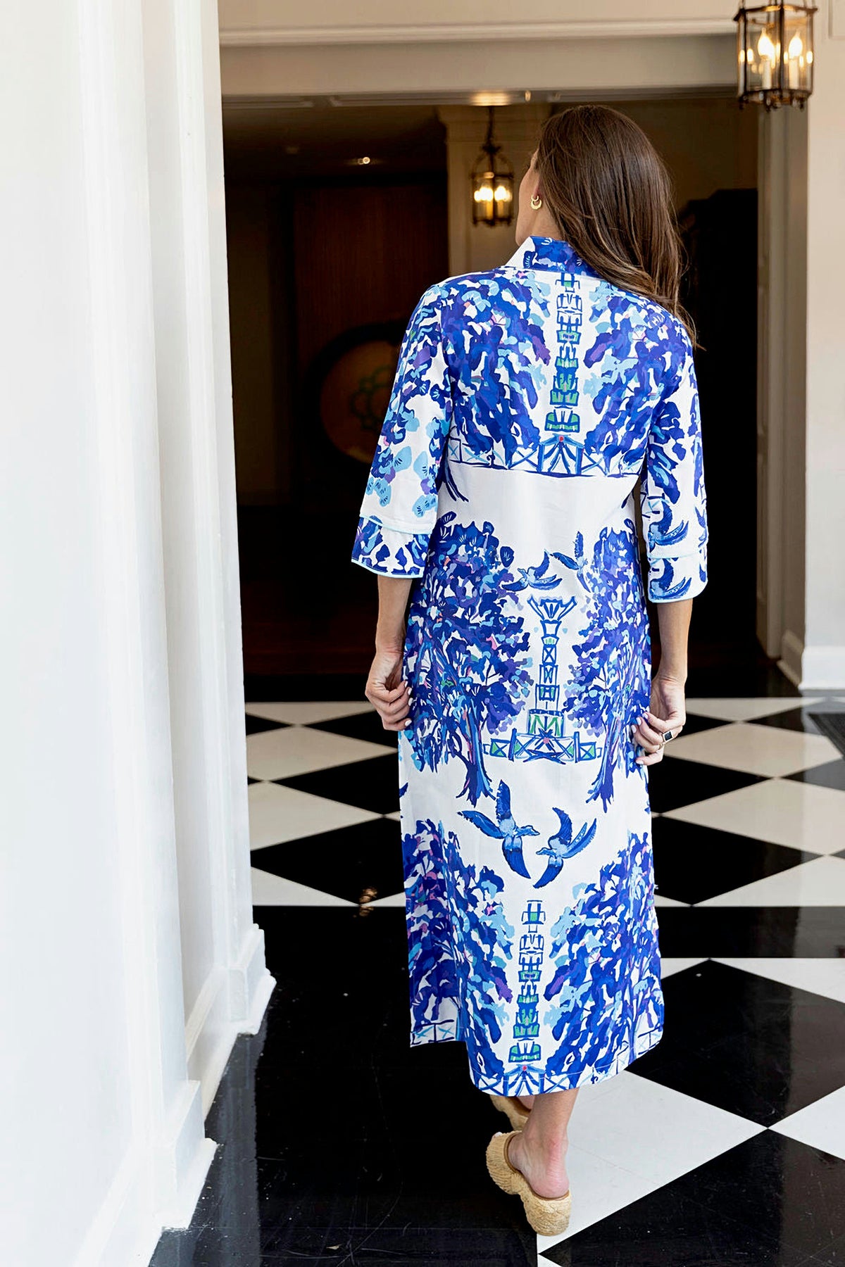 A woman walks down a hallway with a black and white checkered floor in the Willow Bouvier long dress.